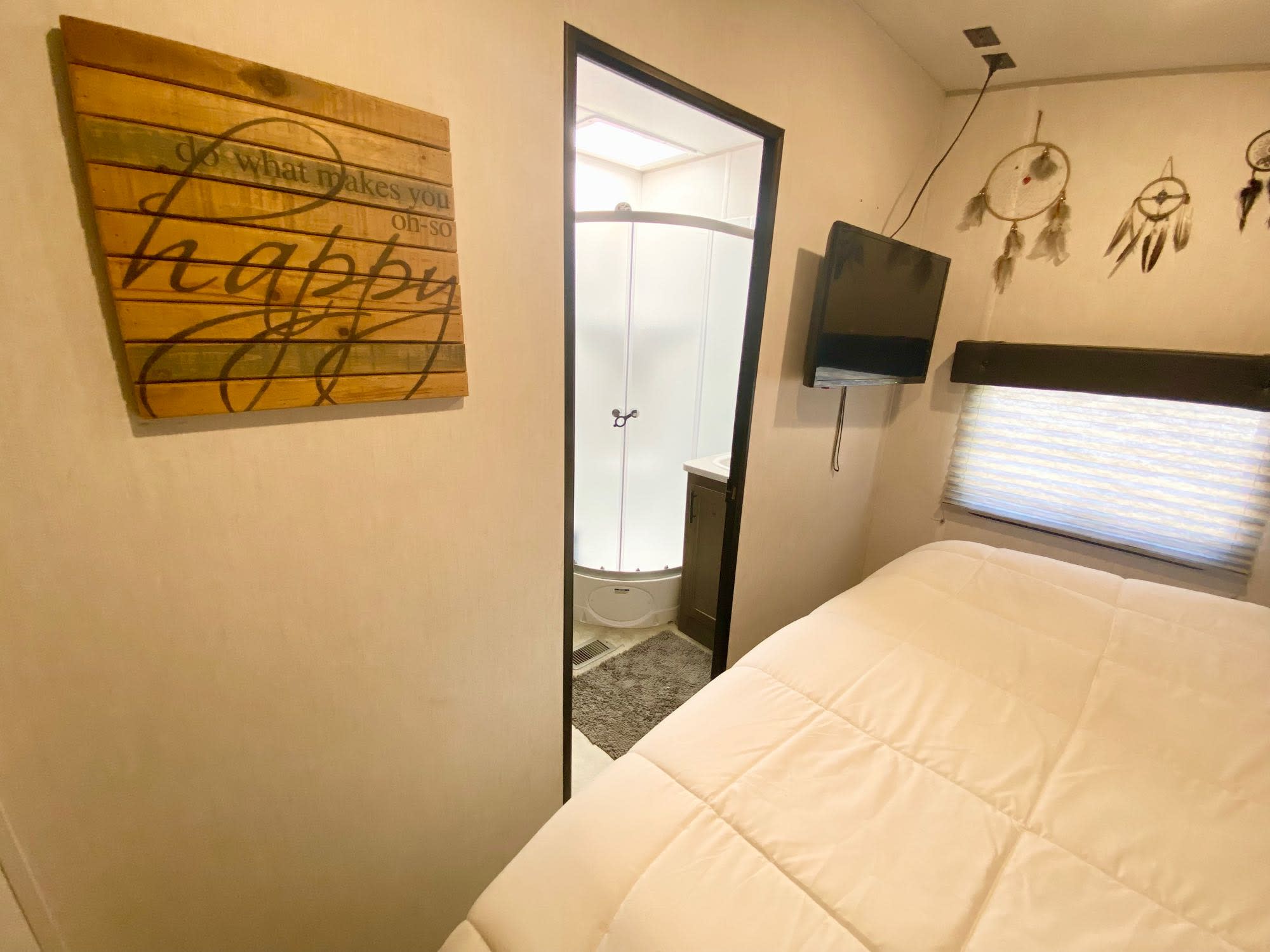 Cozy RV rental bedroom featuring a bed, TV, and dreamcatchers, with an adjacent bathroom visible through an open doorway.. Forest River Vengeance 2021
