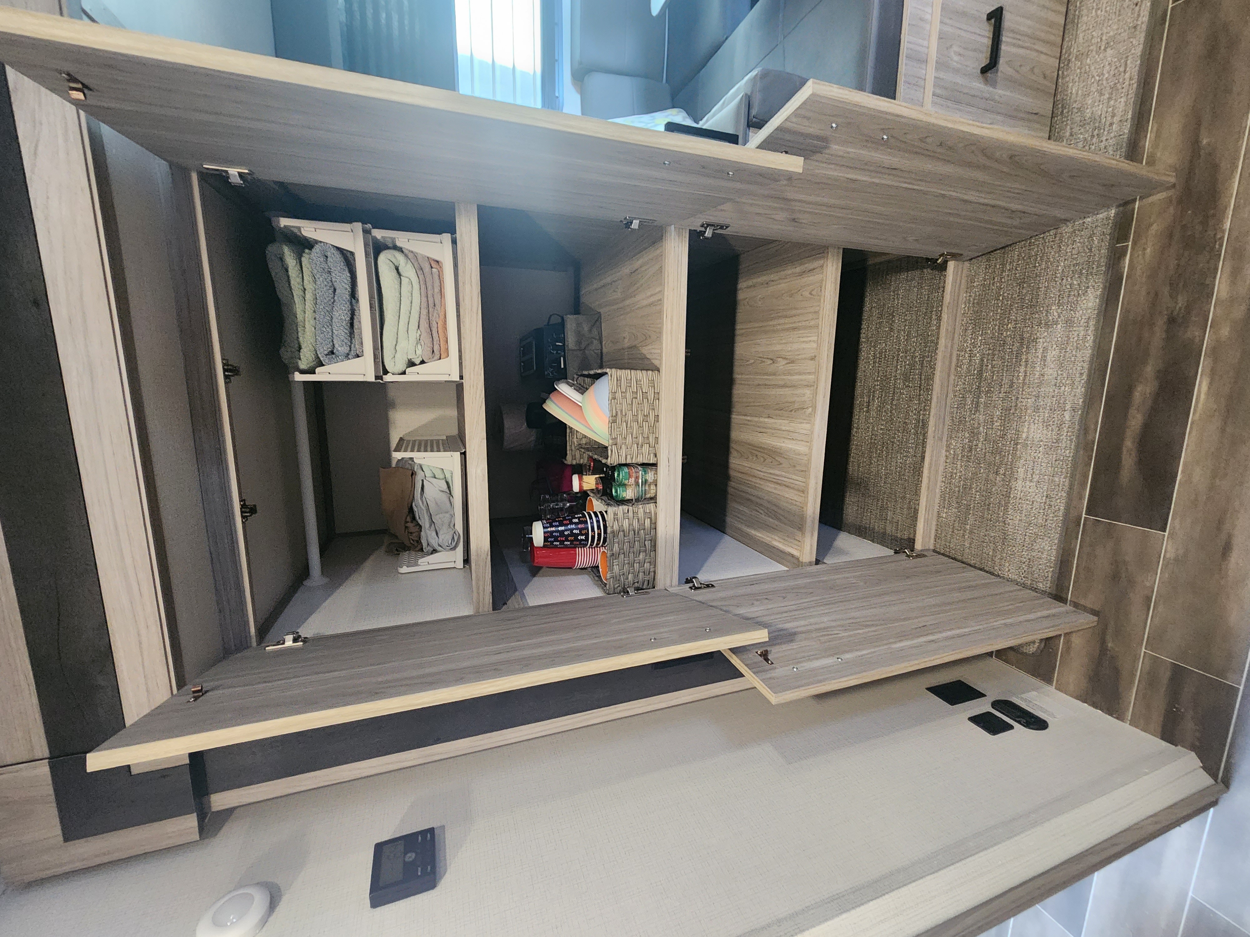 Clever RV rental storage solutions: Open wood-look cabinets reveal organized bins of clothes, baskets, and travel supplies.. Keystone RV Passport SL Ultra Lite 2023