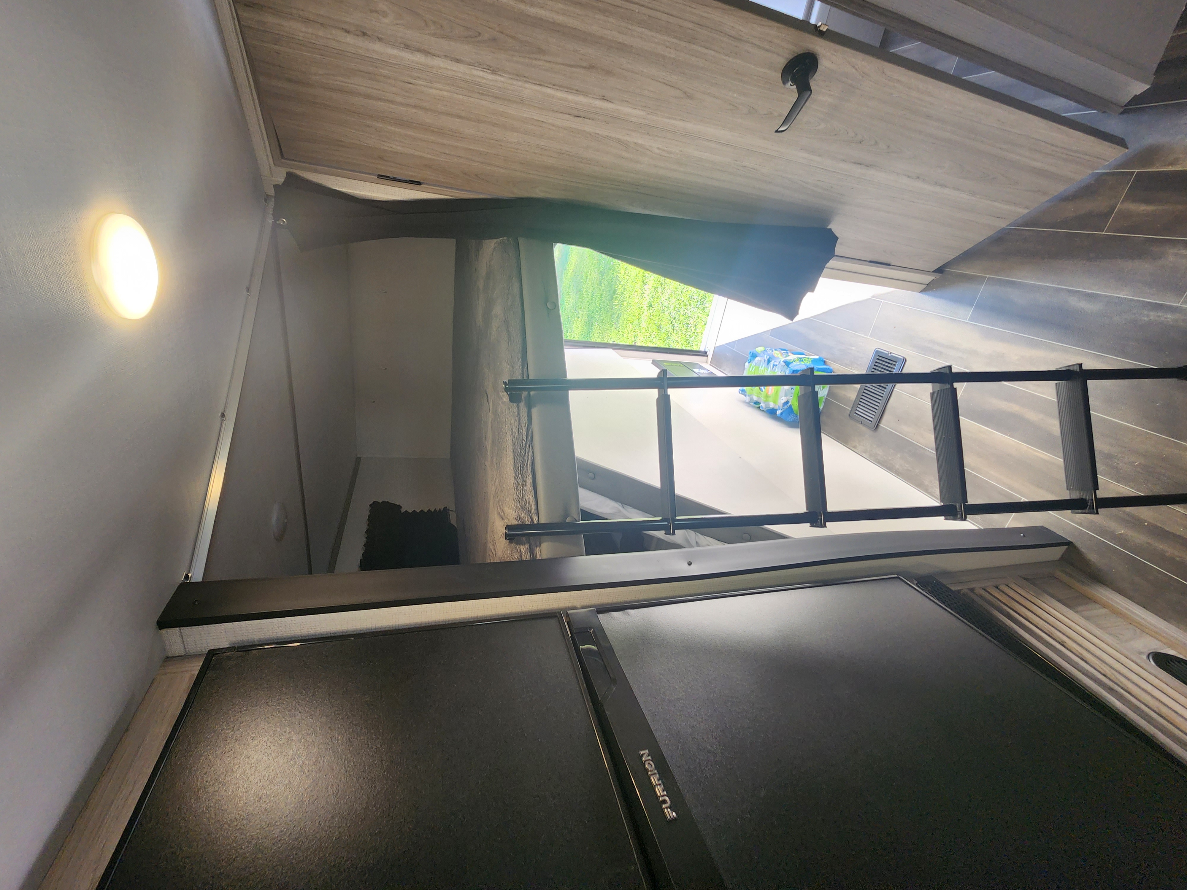 RV rental interior features a bunk bed with ladder, modern wood-look finishes, a bright light, and view to green grass.. Keystone RV Passport SL Ultra Lite 2023