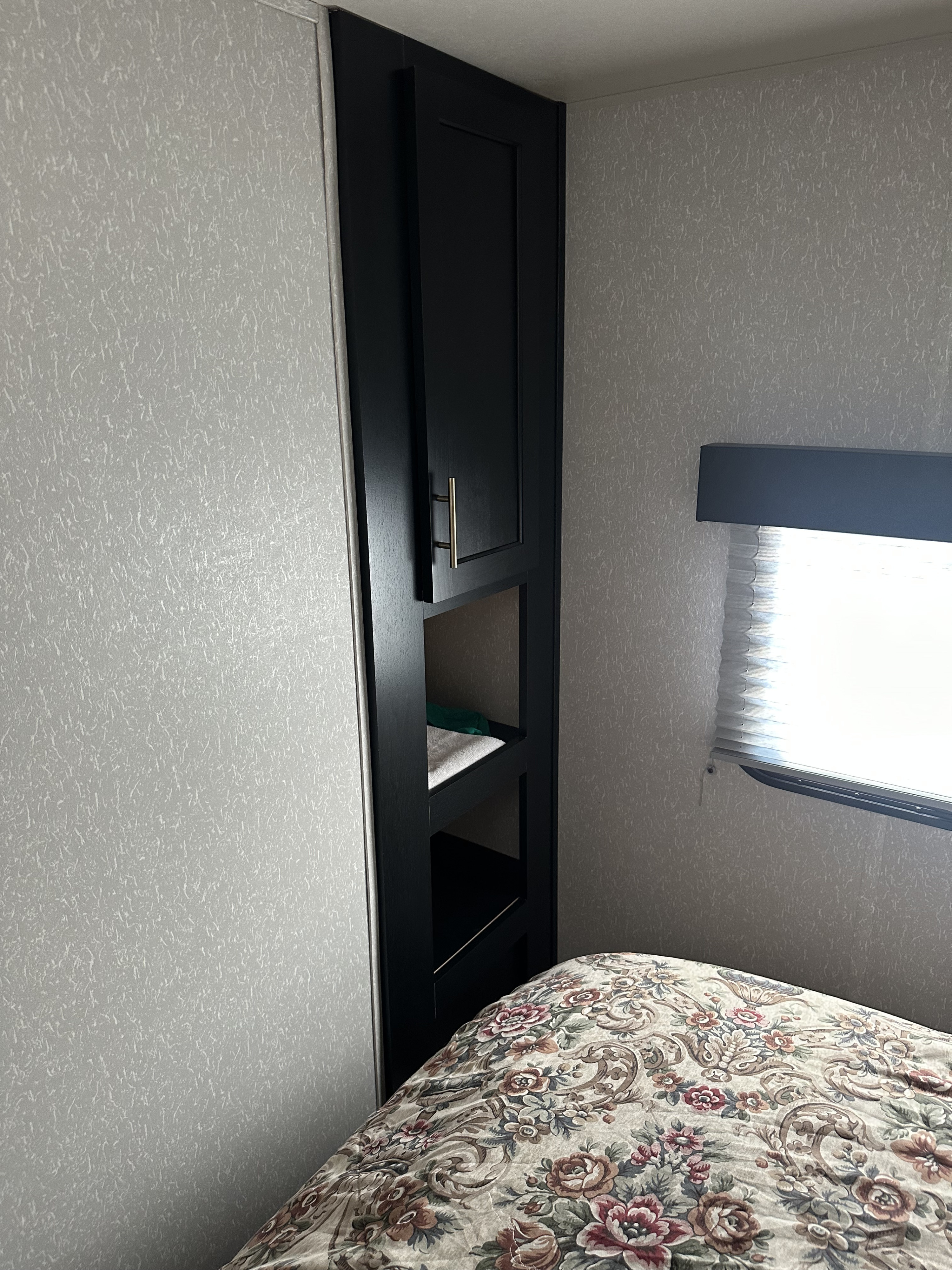 Cozy RV rental bedroom featuring dark built-in storage, a patterned bed, and bright window blinds.. Forest River Cherokee Cherokee Black Label 2022