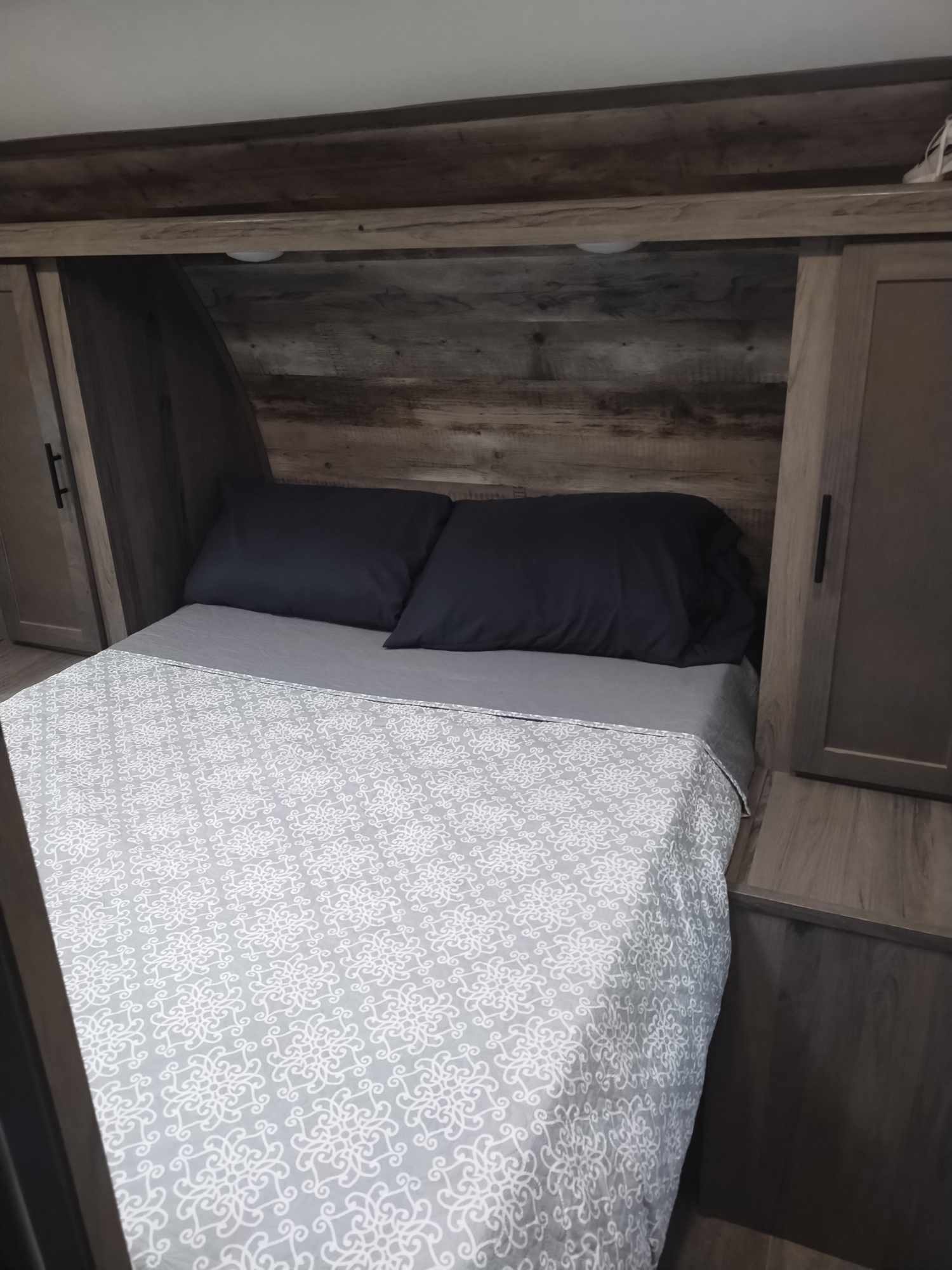 This RV rental bedroom offers a cozy bed, dark pillows, wood paneling, and compact storage for comfortable travel.. Gulf Stream Ameri-Lite 2021