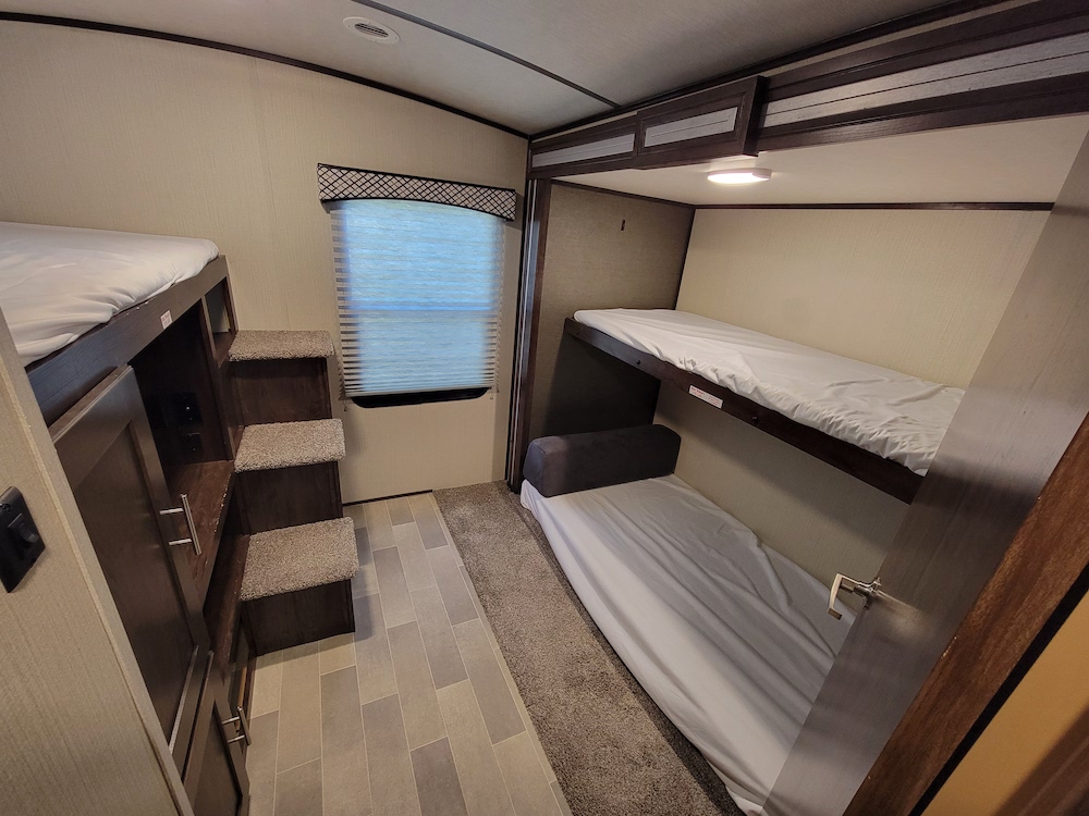 RV rental bunk room with multiple beds, steps, and storage cabinets, offering compact sleeping space.. Cruiser RV Embrace Ultra Lite 2020