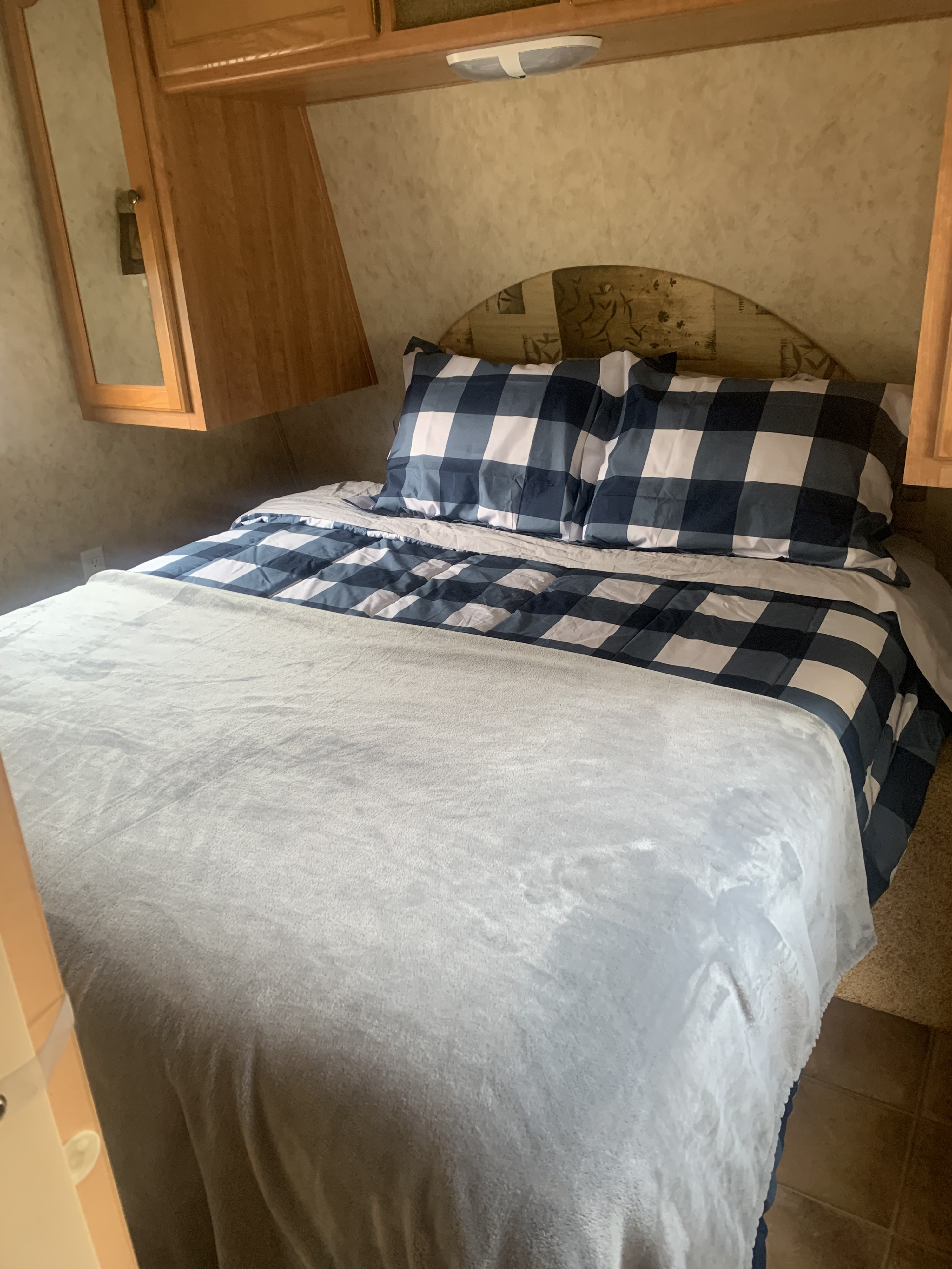 Cozy RV rental bedroom with blue plaid bedding, a light gray blanket, and wooden cabinets, offering a comfortable space.. Keystone RV Springdale 2008