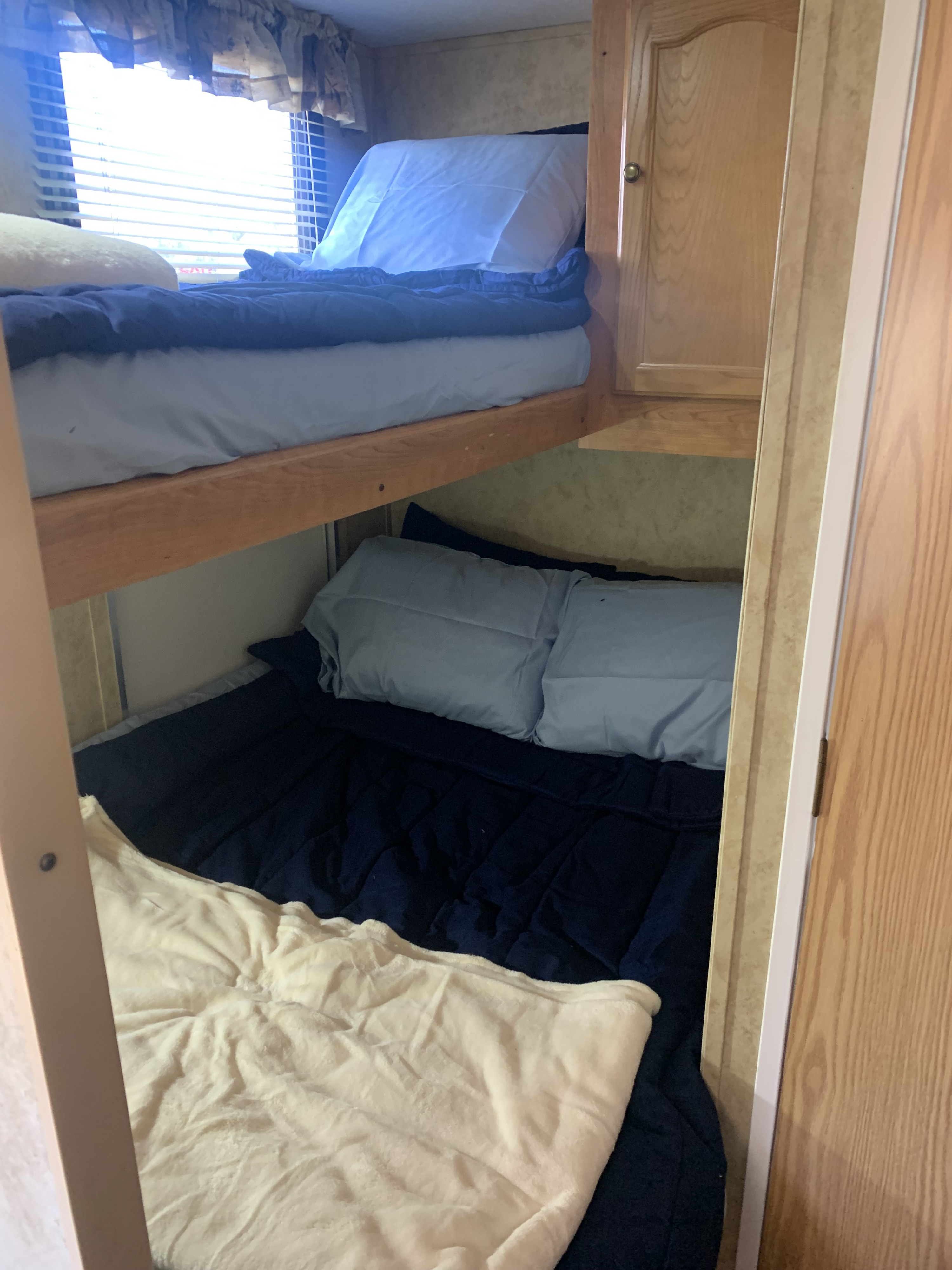 Cozy bunk beds inside an RV rental, featuring blue bedding, a window, and wooden interior for comfortable sleeping.. Keystone RV Springdale 2008