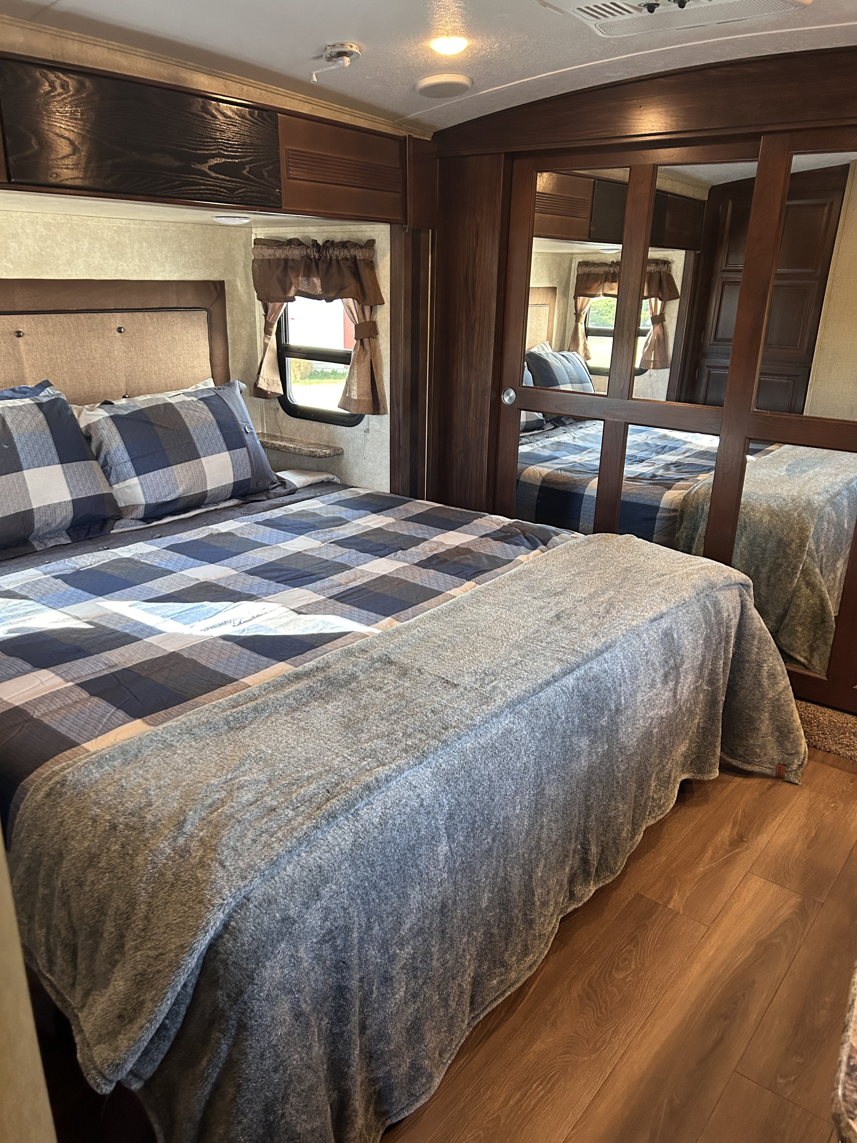 Cozy RV rental bedroom features a comfy bed with blue plaid linens, mirrored closet, and warm wood tones.. Keystone RV Montana Mountaineer 2015