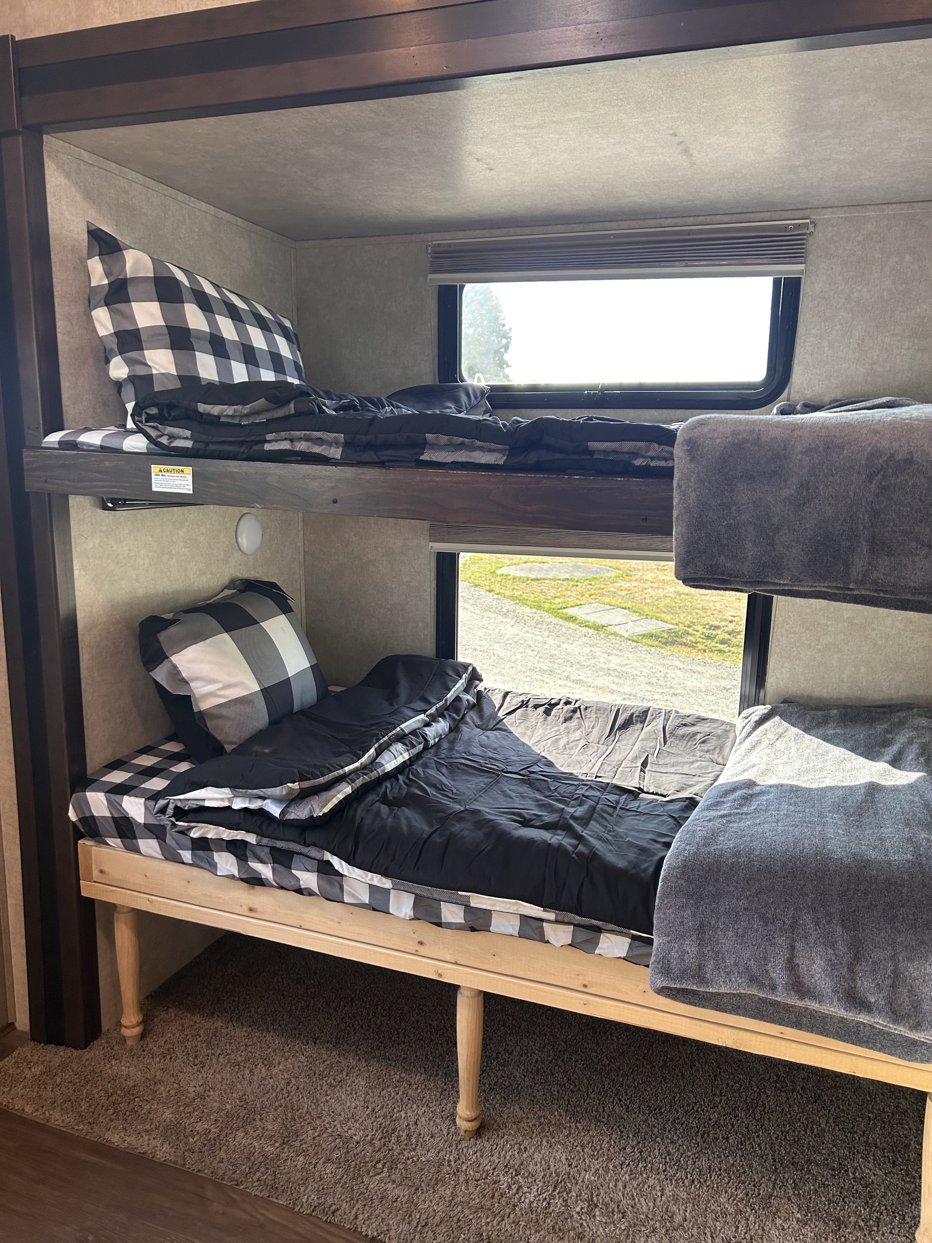 RV rental bunk beds detailed: cozy buffalo check bedding & soft blankets in a travel trailer interior, bright window view.. Keystone RV Montana Mountaineer 2015