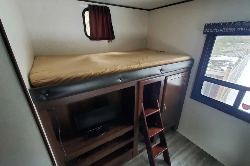 RV rental bedroom with elevated bunk bed, built-in storage, TV, and an access ladder.. Jayco Jay Flight SLX 2018