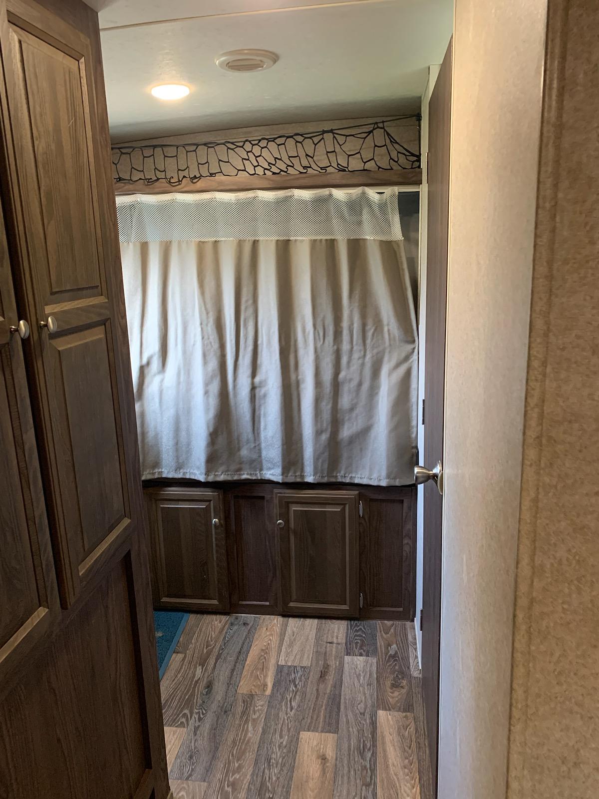 RV rental interior view: Dark wood cabinets, light curtain (likely hiding bed), wood-look floor, and overhead light fixture.. Forest River Flagstaff Shamrock 2016
