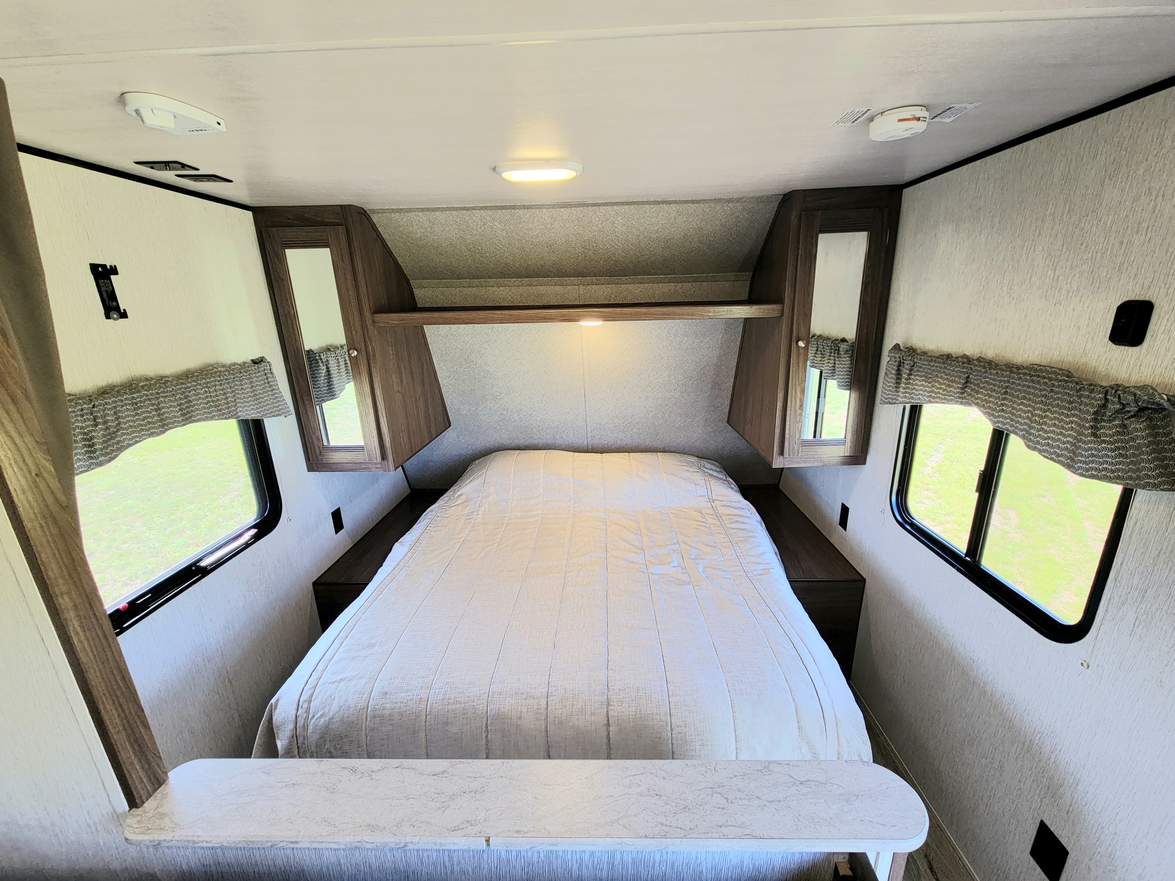 Cozy RV rental bedroom featuring a comfortable bed, mirrored overhead cabinets, and two large windows for natural light.. Heartland Prowler 2018