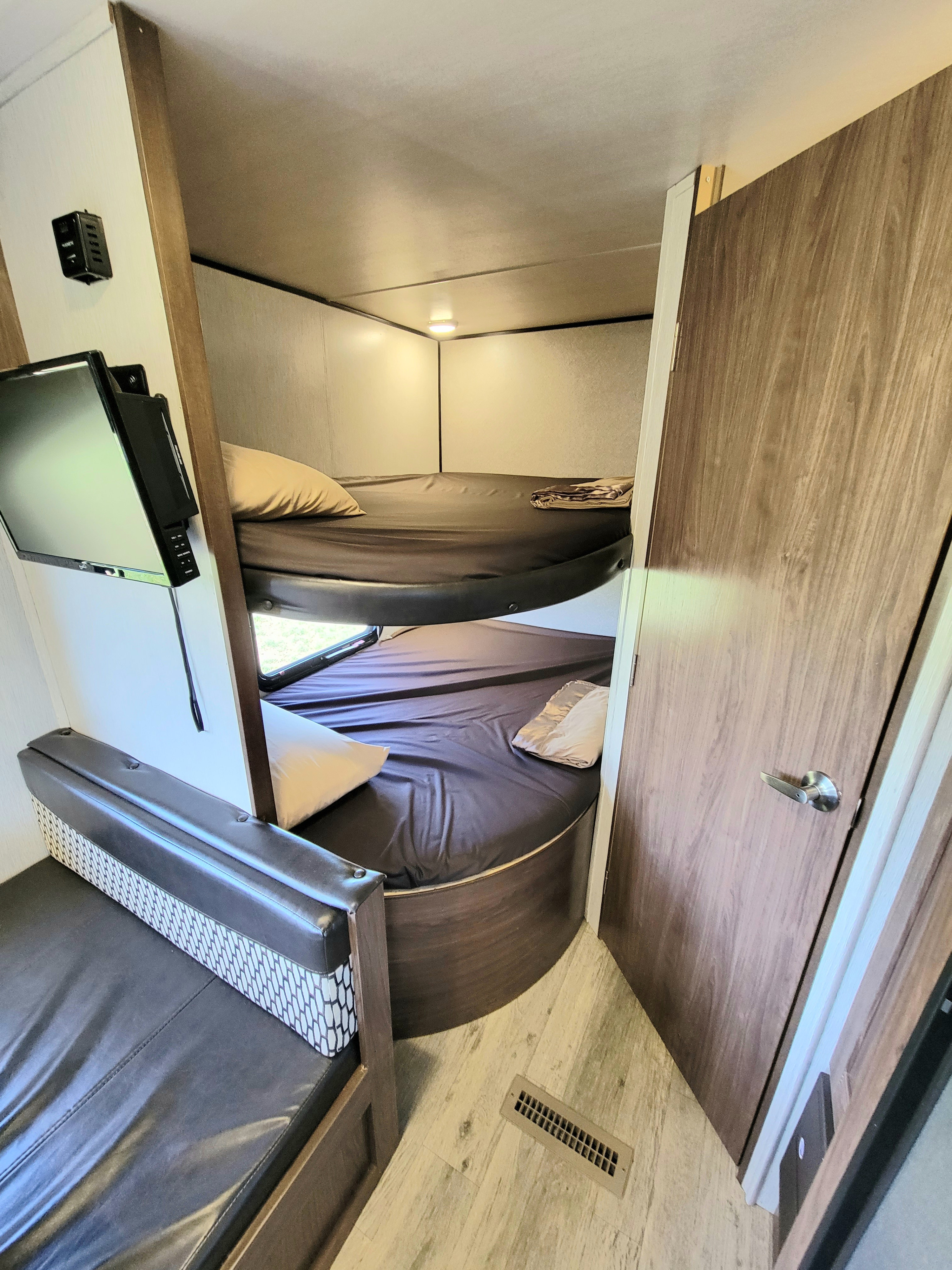 This RV rental interior shows a sleeping area with stacked bunk beds, a wall-mounted TV, and a comfortable bench seat.. Heartland Prowler 2018
