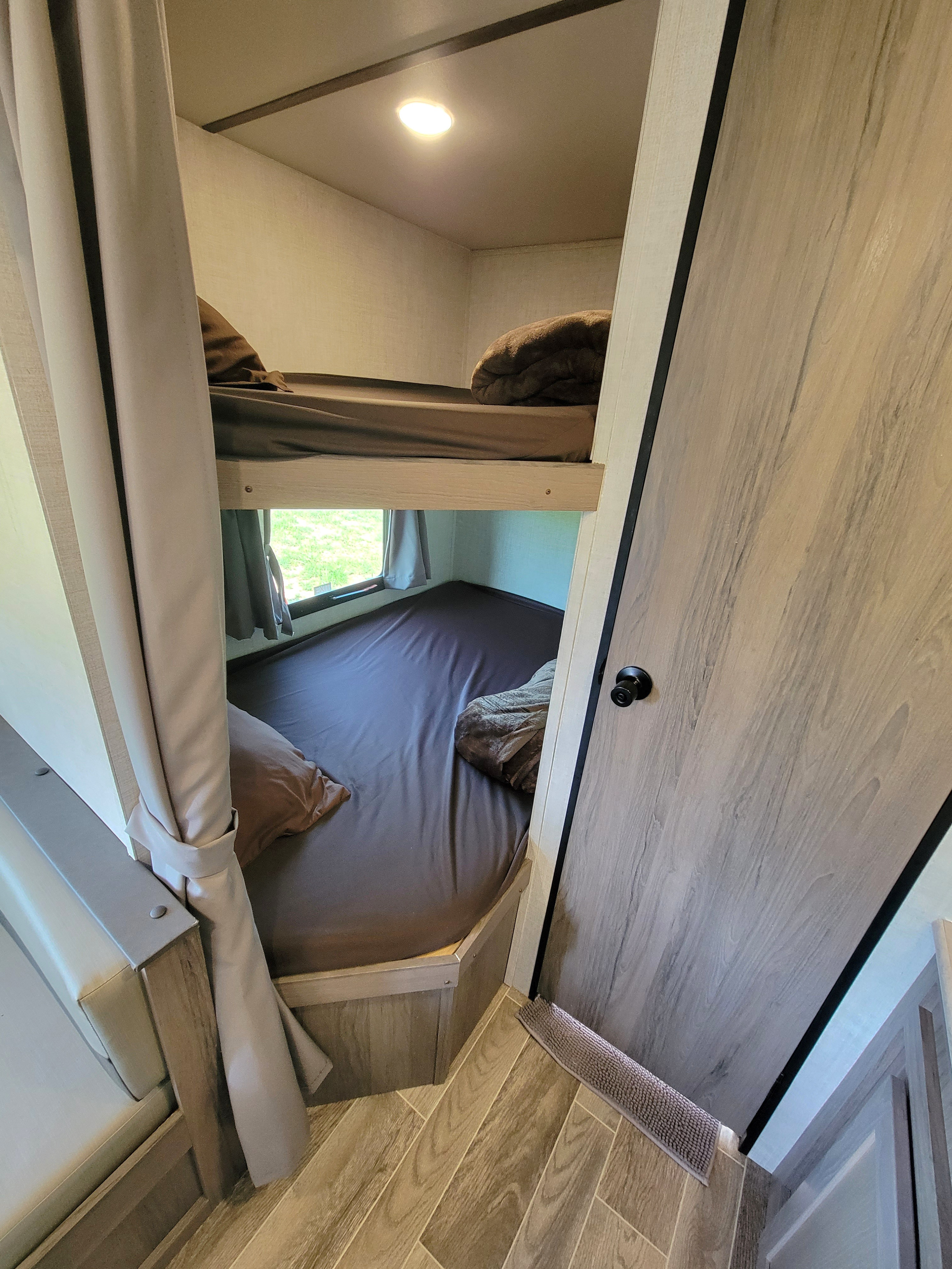 Cozy RV rental bunk beds with a window view, perfect for family camping and travel adventures.. Gulf Stream Enlighten 2022