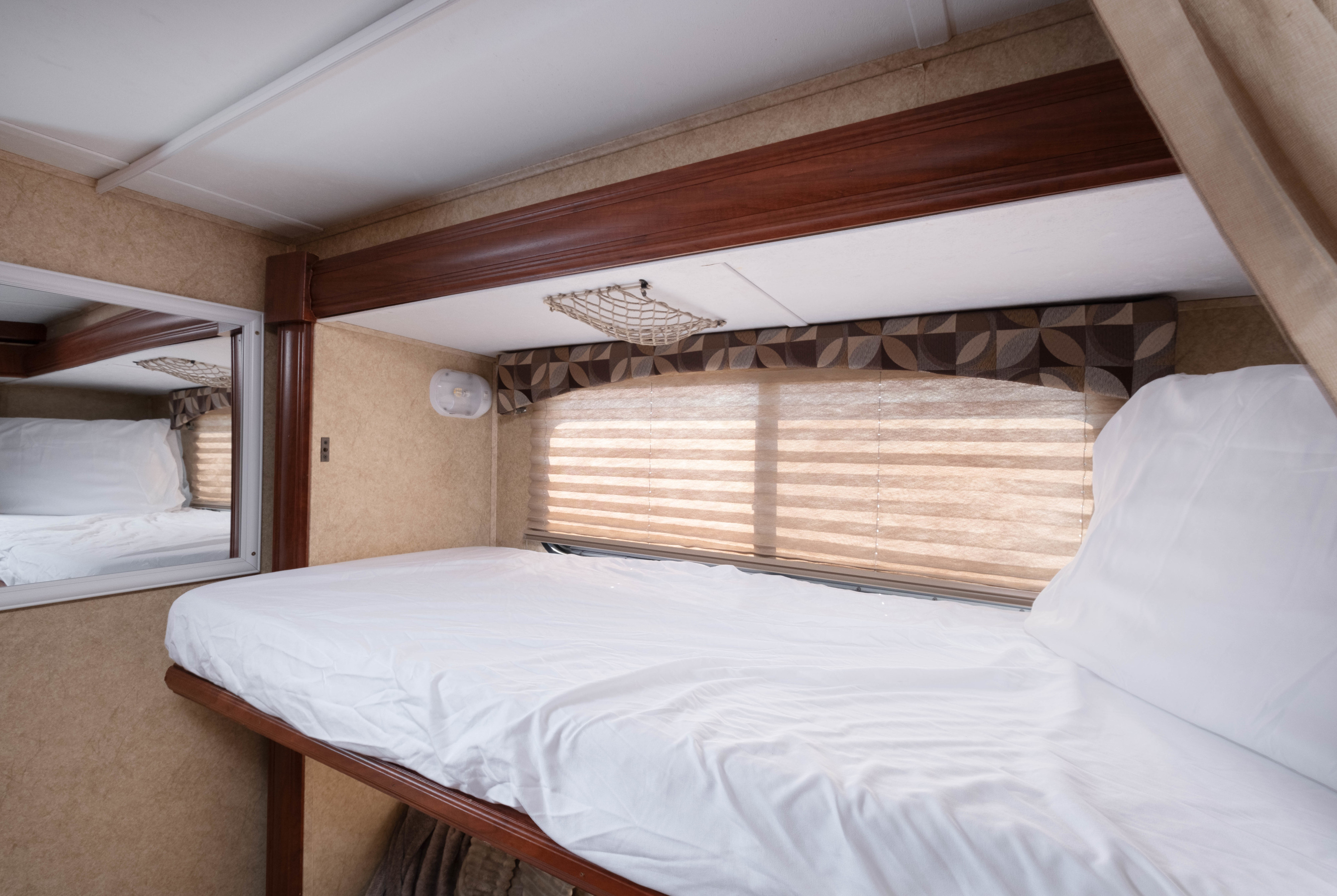 Cozy sleeping area in an RV rental, featuring a bunk bed with white sheets, mirror, and window blinds.. Forest River Sunseeker 2013