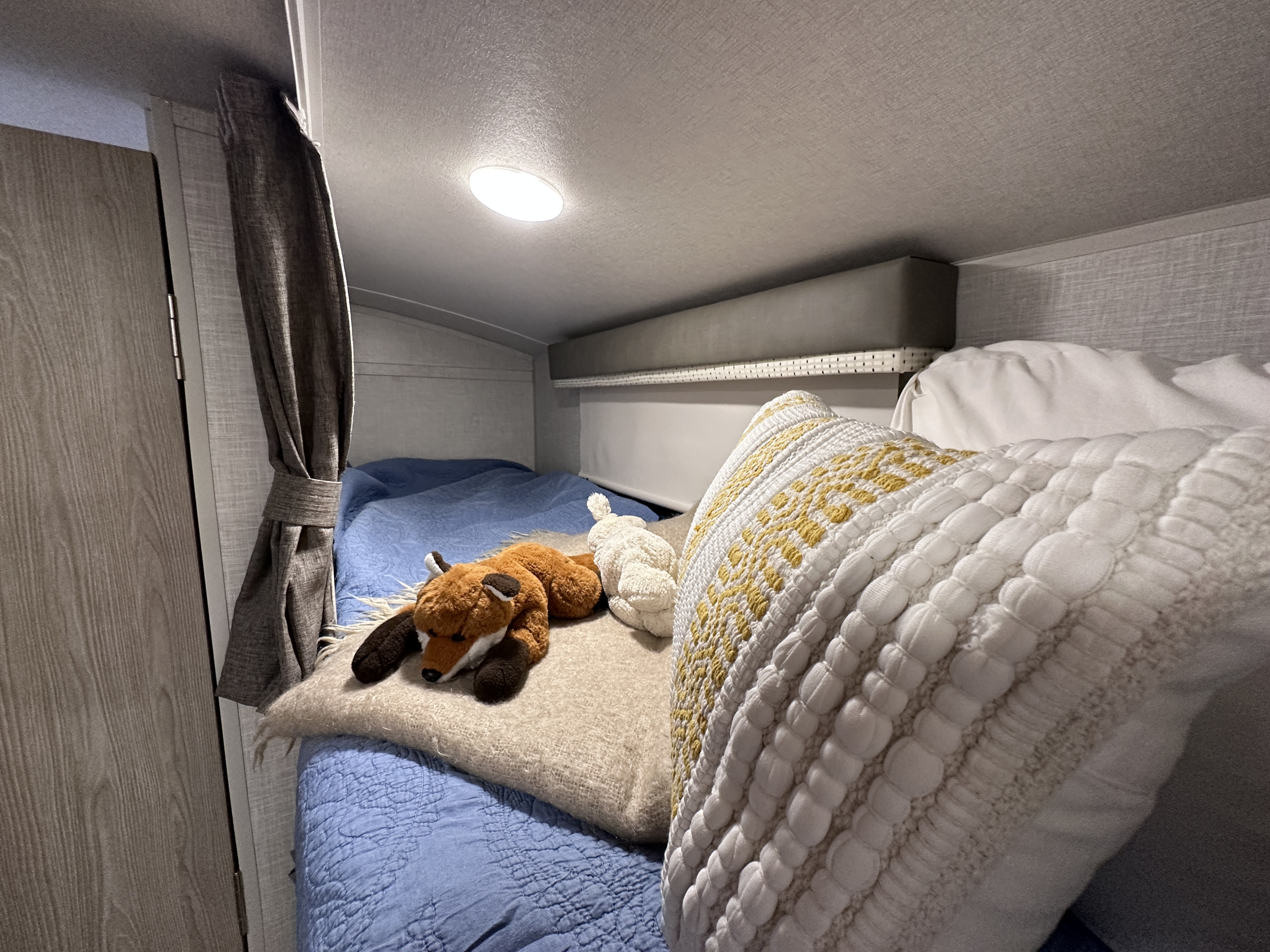 Inside an RV rental: a cozy bunk bed with blue bedding, a fox and rabbit plush, and a decorative pillow.. Forest River Rockwood Geo Pro 2021
