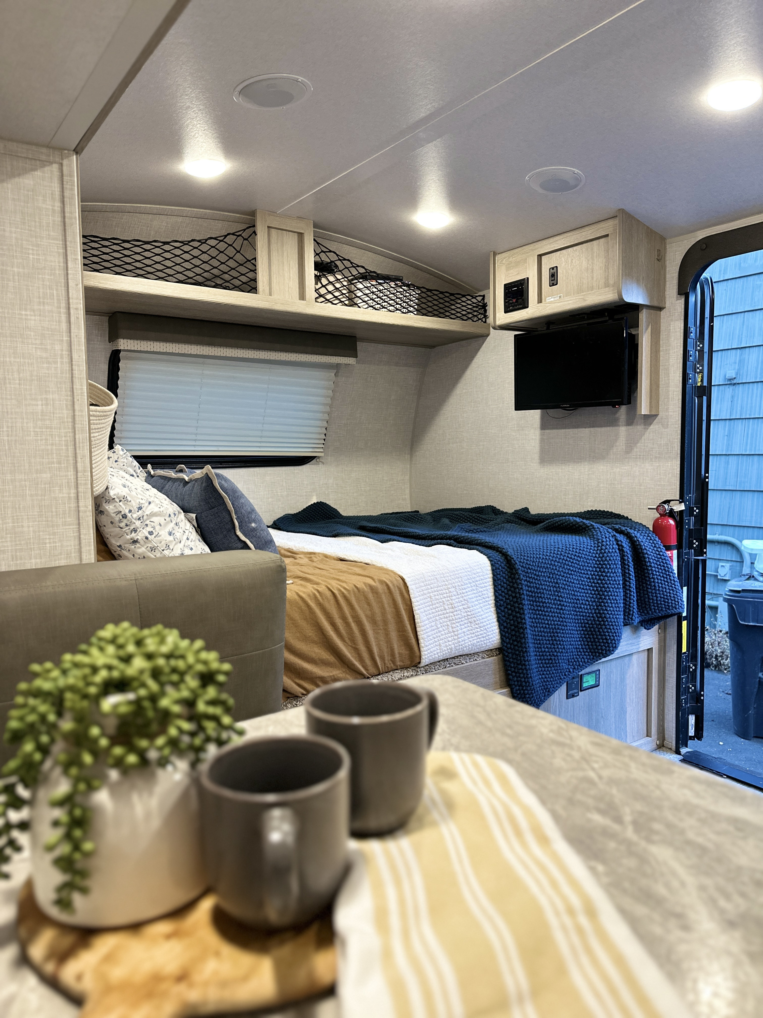 Inside a modern RV rental: a cozy bed with blankets, mounted TV, and netted overhead storage for compact living.. Forest River Rockwood Geo Pro 2021