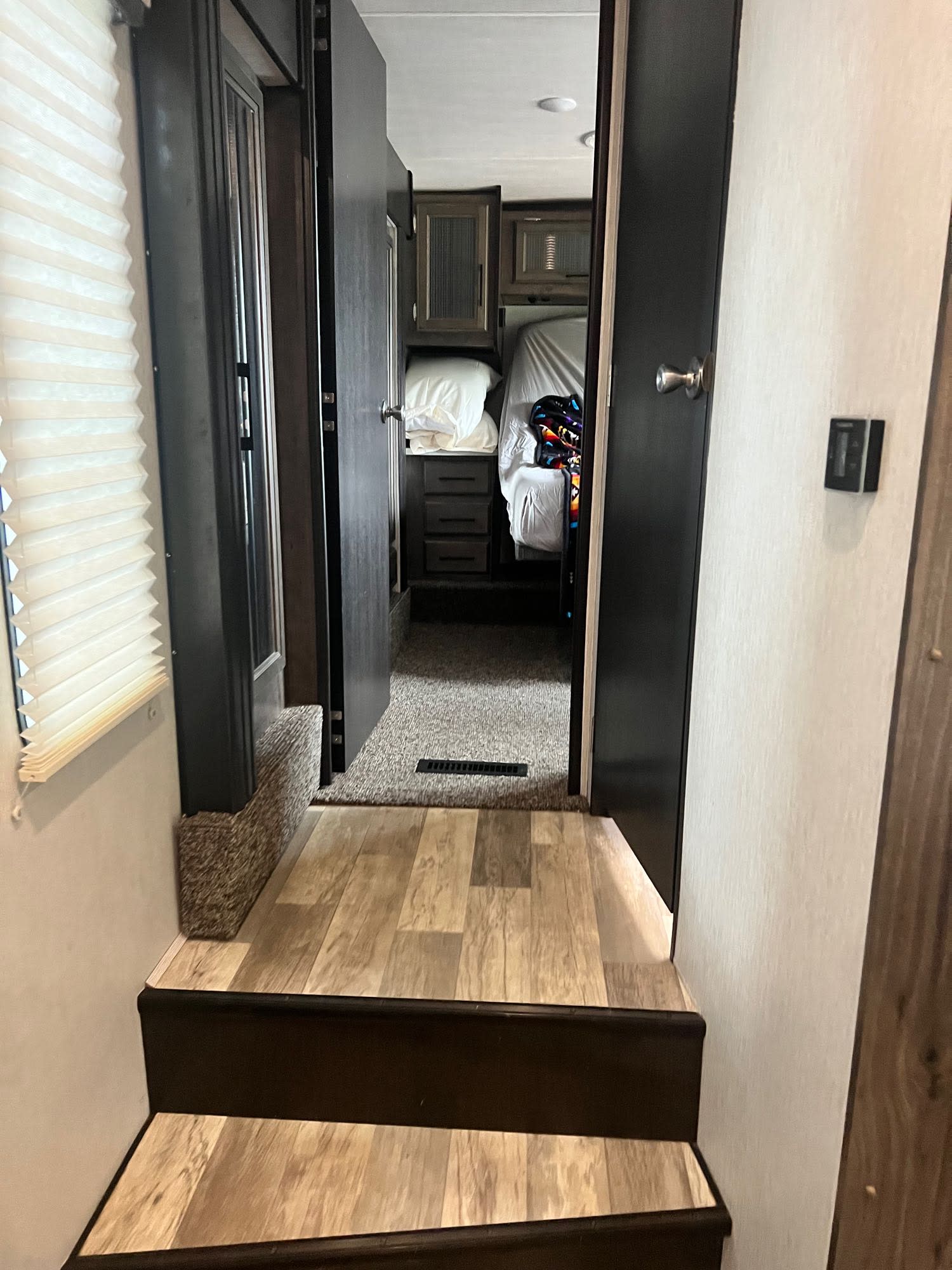 Inside an RV rental, steps lead up to a hallway that opens into a cozy bedroom with a bed, dresser, and cabinets.. Heartland Torque 2020