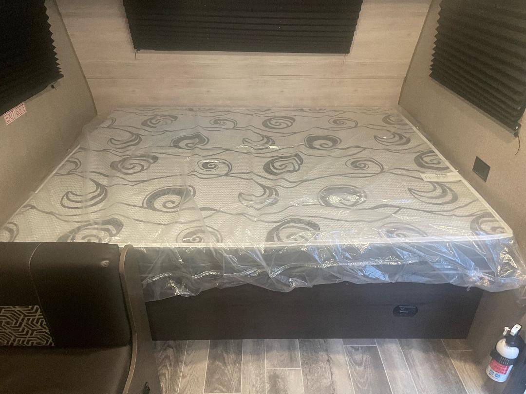 Spacious RV rental bed area with new mattress in plastic cover, built-in storage, and fire extinguisher. Ideal RV interior.. Jayco Jay Flight SLX Baja Edition 2021