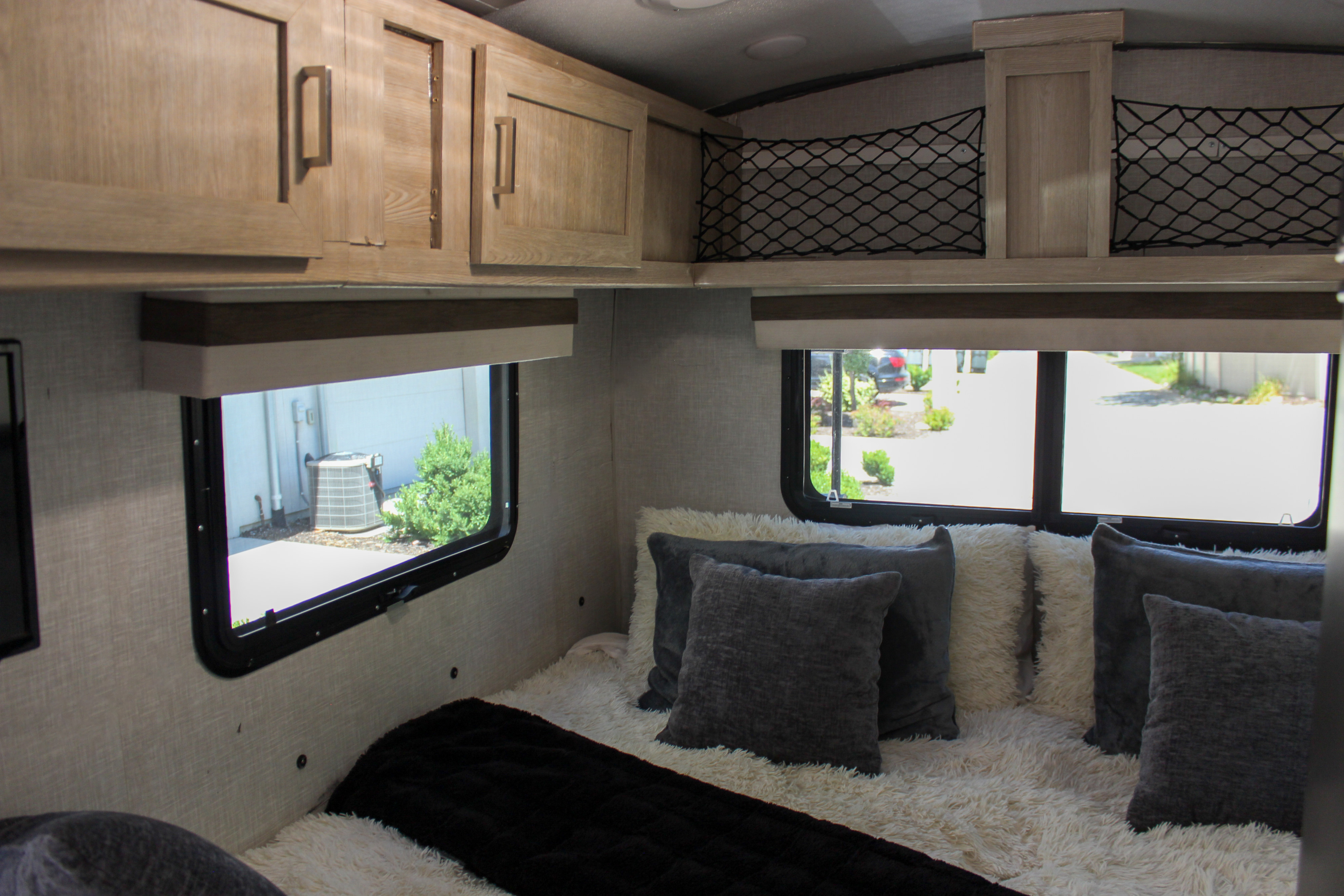 Inside an RV rental: view of a bed with cozy pillows, windows, and practical overhead storage nets.. Forest River Rockwood Geo Pro 2022