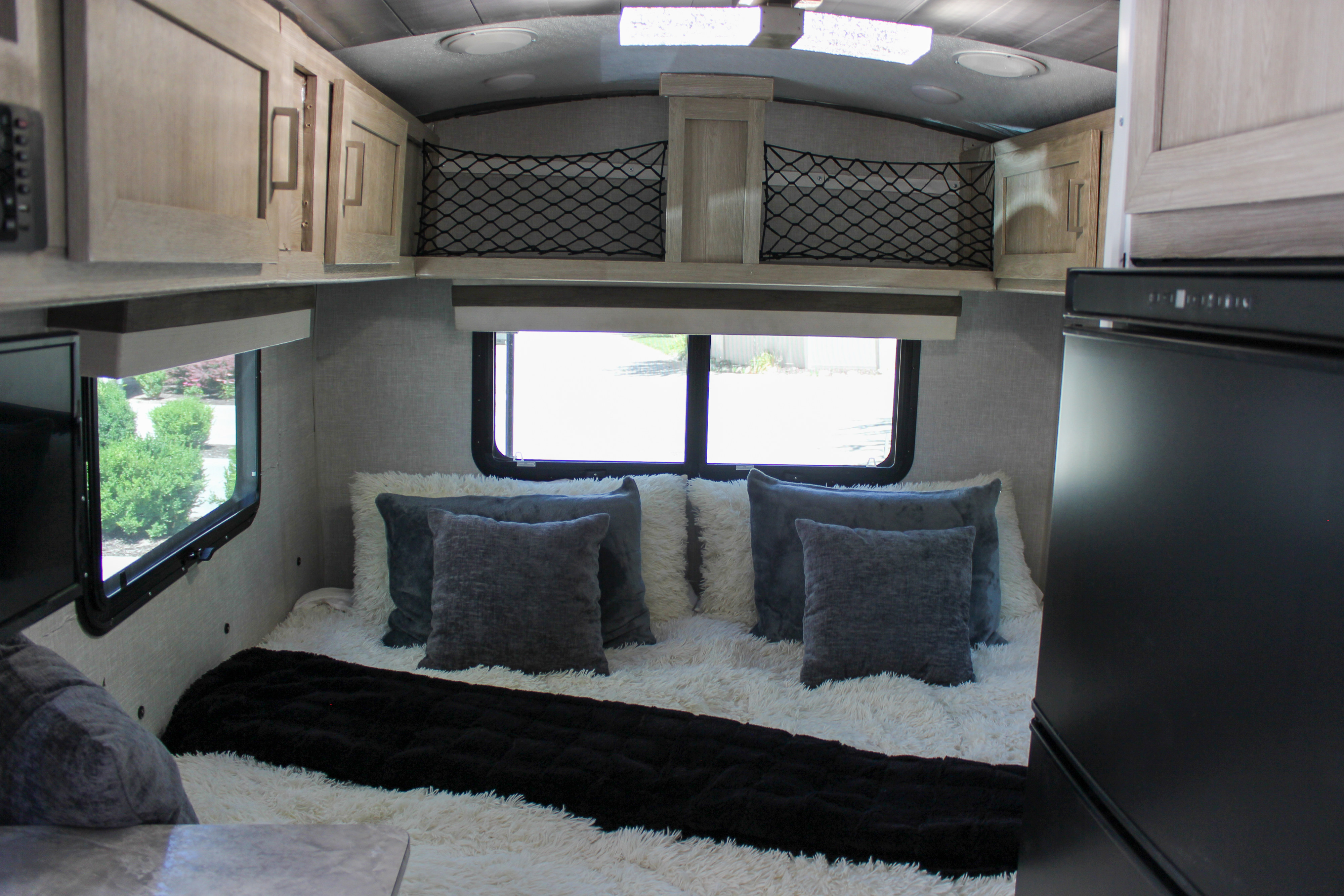Cozy RV rental bedroom featuring a plush bed with white and gray pillows, overhead storage, and windows with outdoor views.. Forest River Rockwood Geo Pro 2022