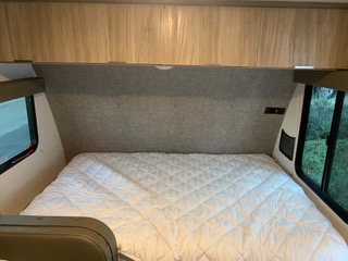 This RV rental offers a compact bedroom with a quilted bed, overhead cabinets, and side windows, ready for your next adventure.. Winnebago Minnie Winnie 2021