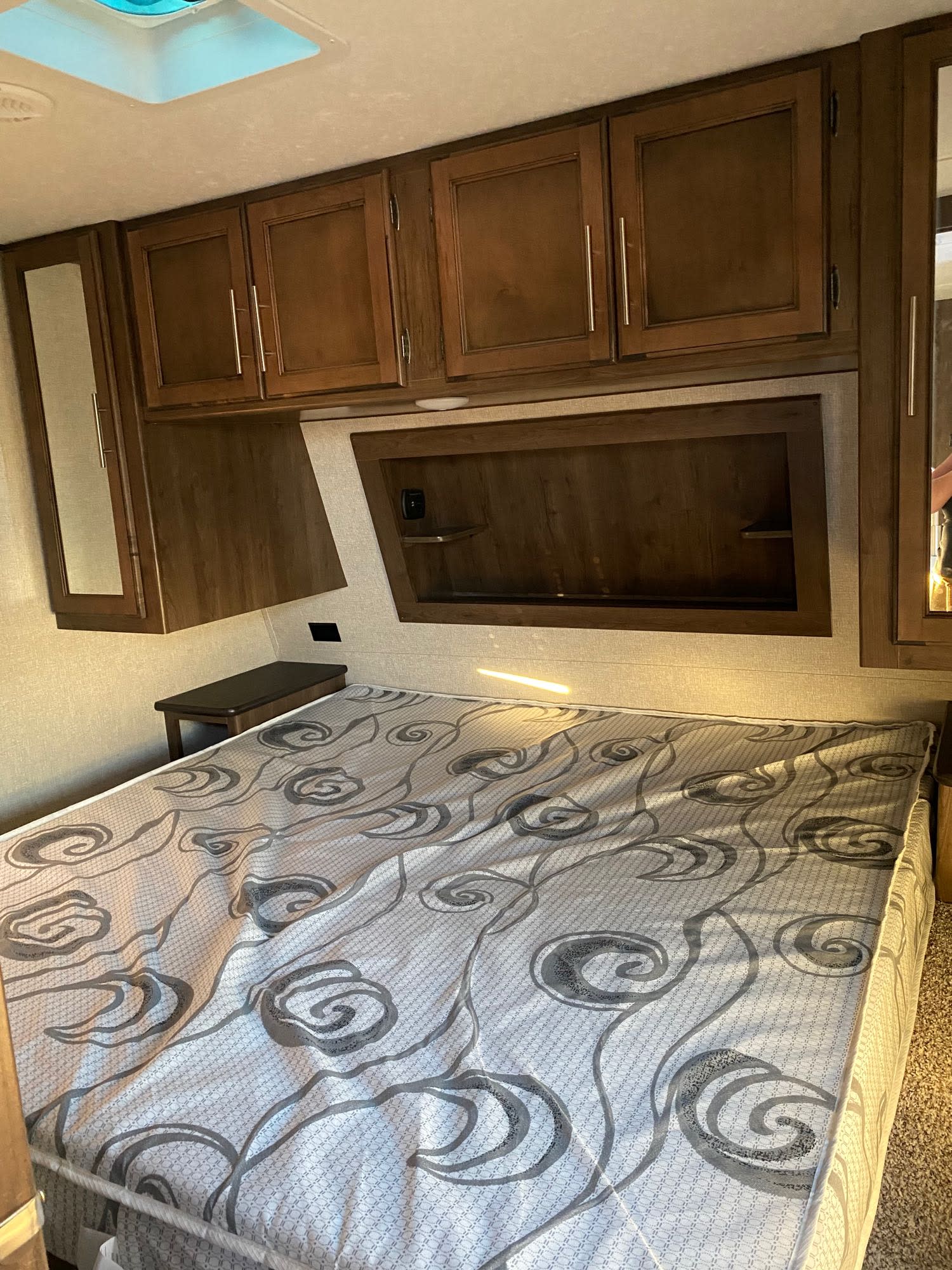 Interior view of an RV rental bedroom featuring a patterned bed, overhead storage cabinets, and a compact bedside table.. Keystone Cougar Half-Ton 2018