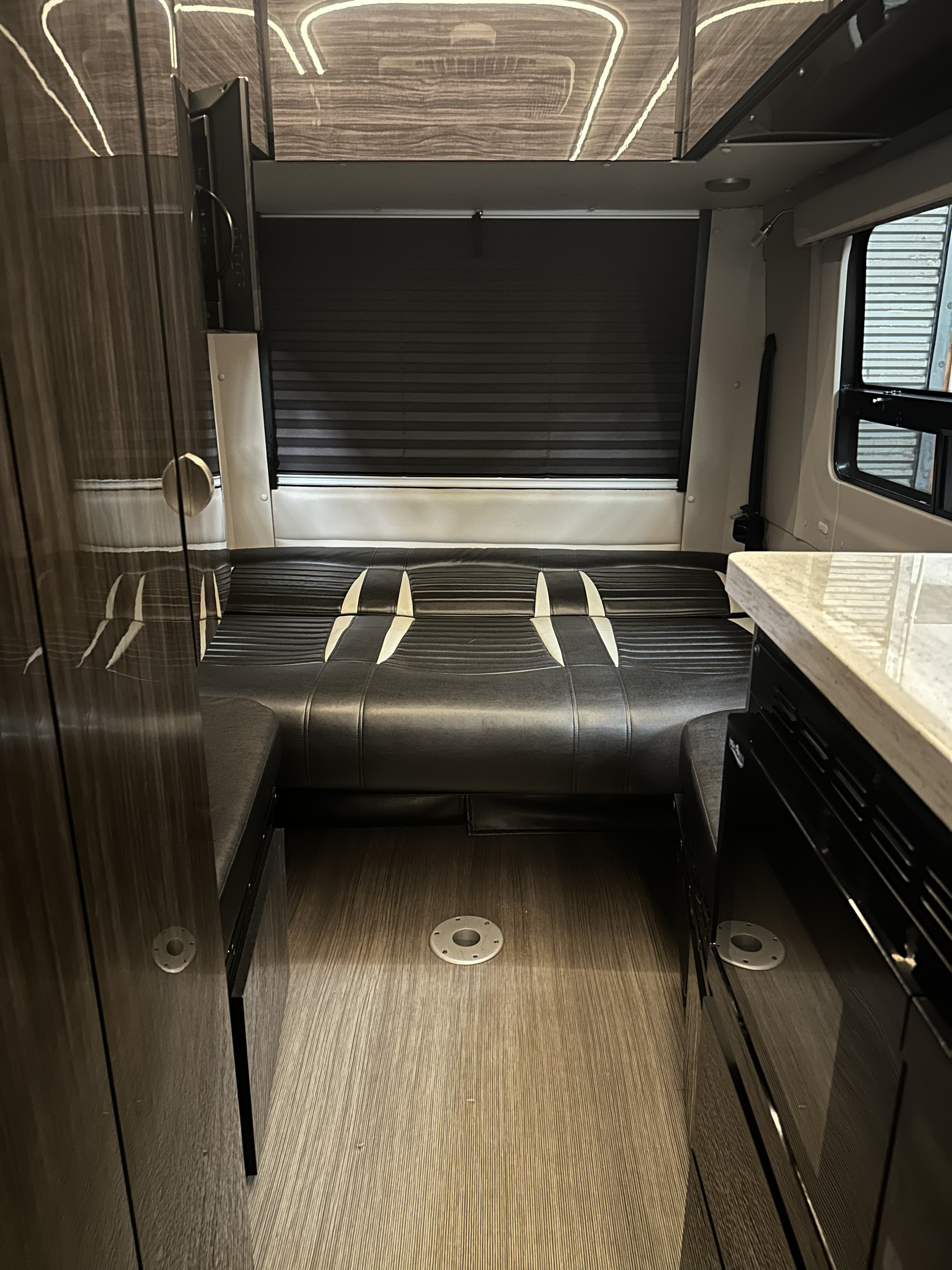 An RV rental interior featuring a convertible seating area, dark window blinds, modern countertop, and wood-look flooring.. Winnebago Era 2017