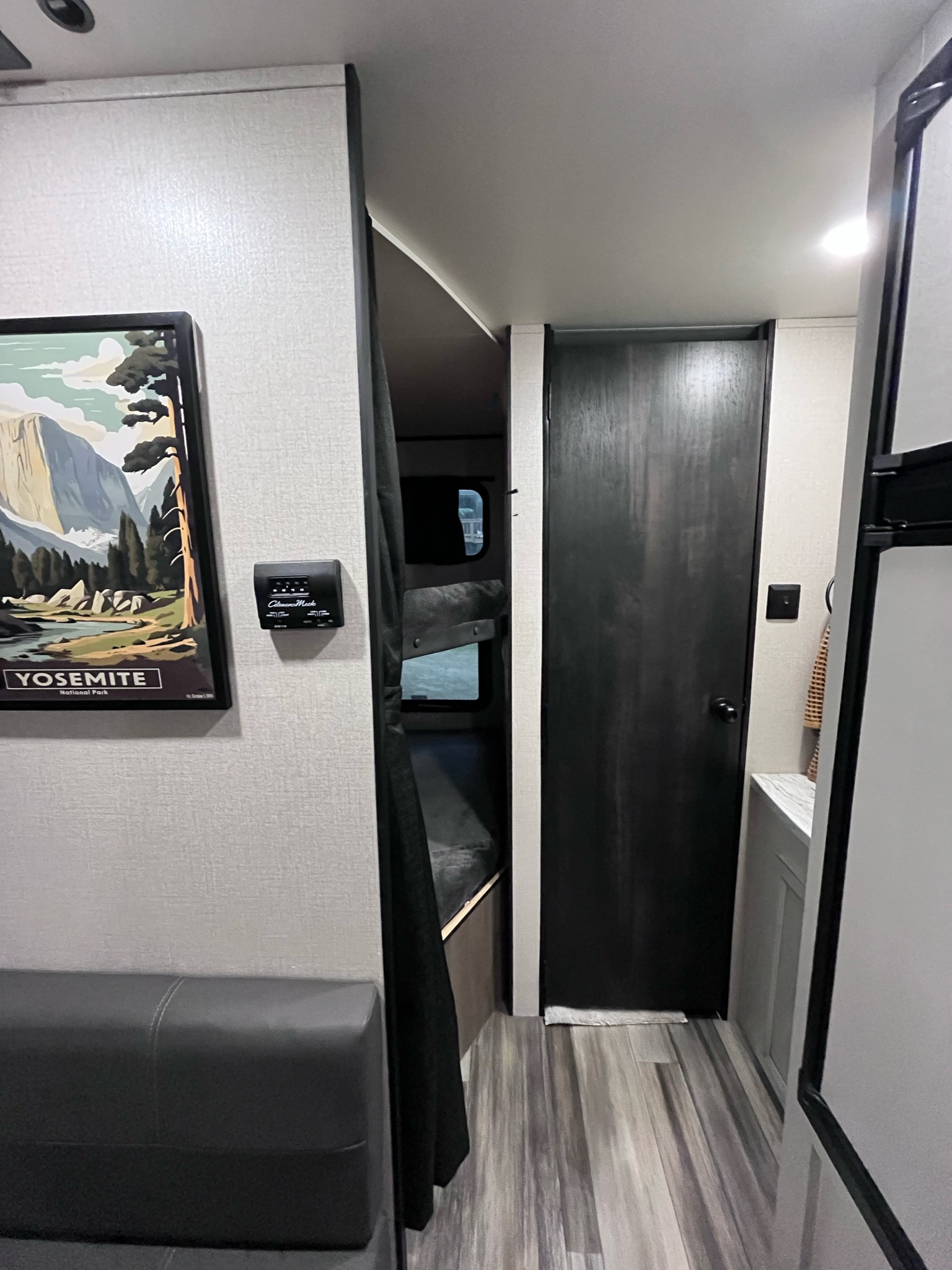 RV rental interior: A Yosemite print & thermostat on the wall, dark curtain to bunk beds, and a black door to the right.. Highland Ridge RV Open Range 2022