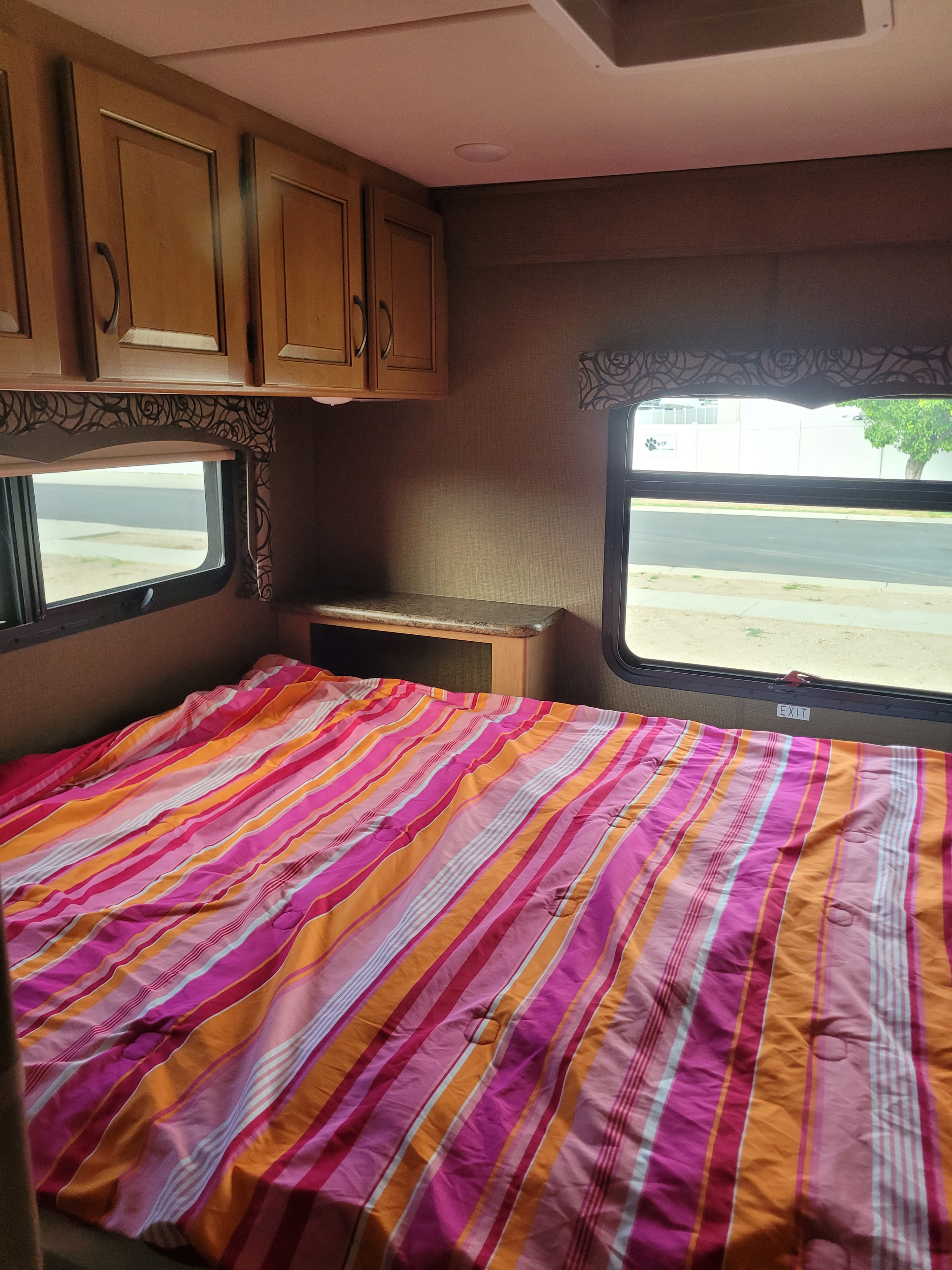Cozy RV rental bedroom featuring a vibrant striped bed, wood cabinets, and large windows revealing the outside.. Thor Four Winds 2017