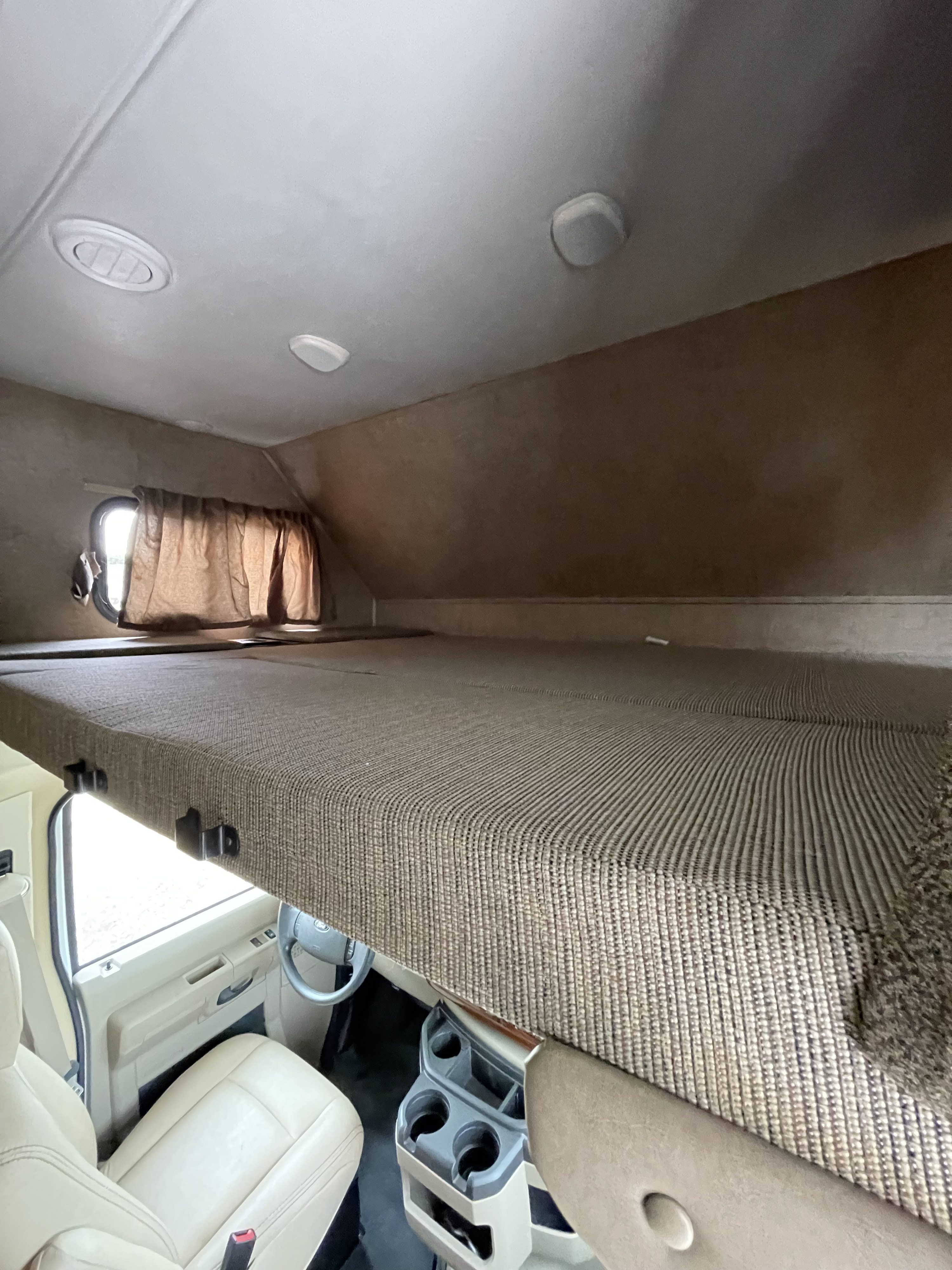 Spacious RV rental interior featuring a comfy cab-over bunk bed above the driver's cockpit with window views.. Forester Forester Motorhome 2016
