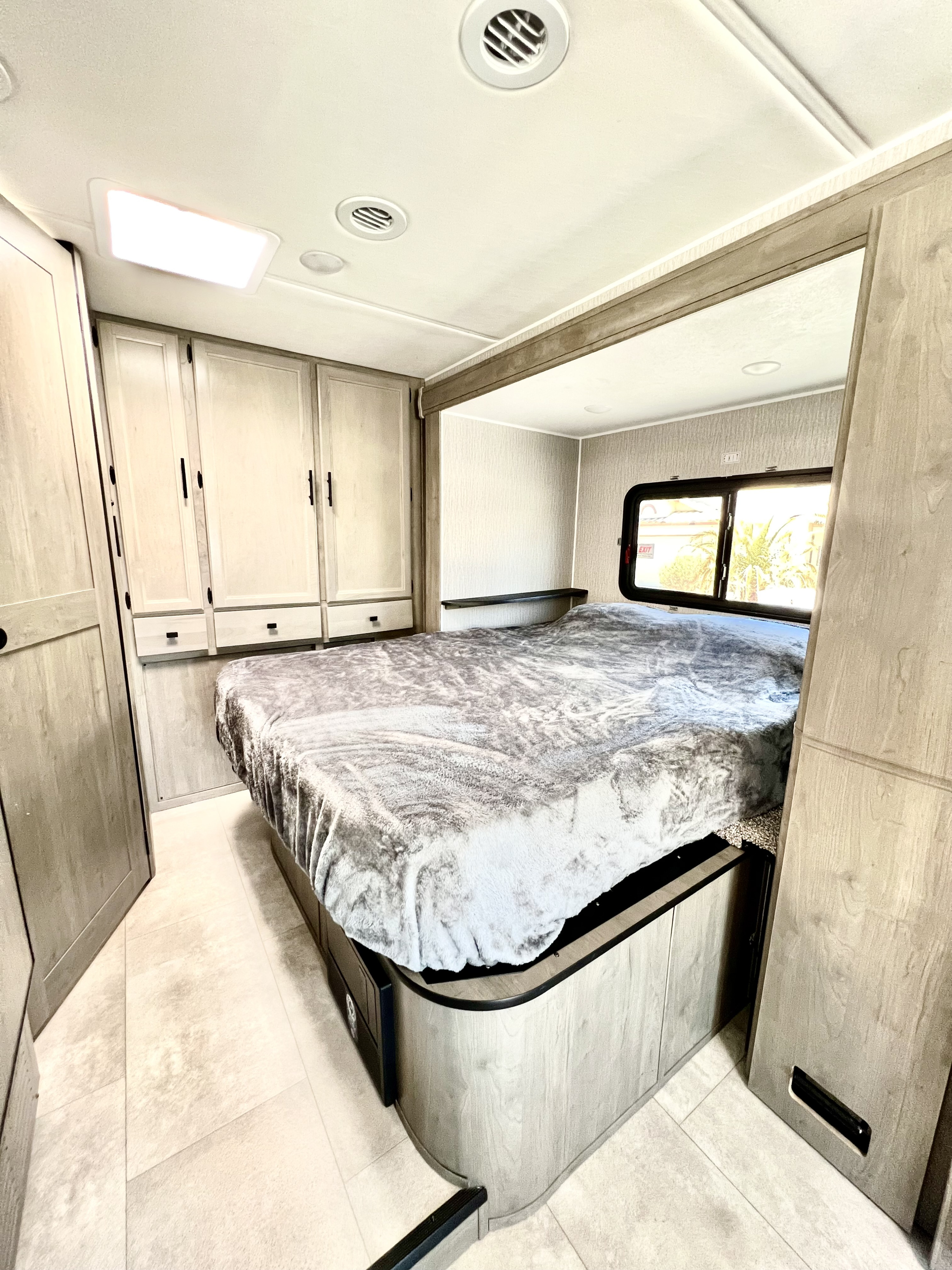 Experience comfort in this modern RV rental bedroom, featuring a cozy bed, ample cabinets, and a bright window.. Coachmen Prism Elite 24FS 2023