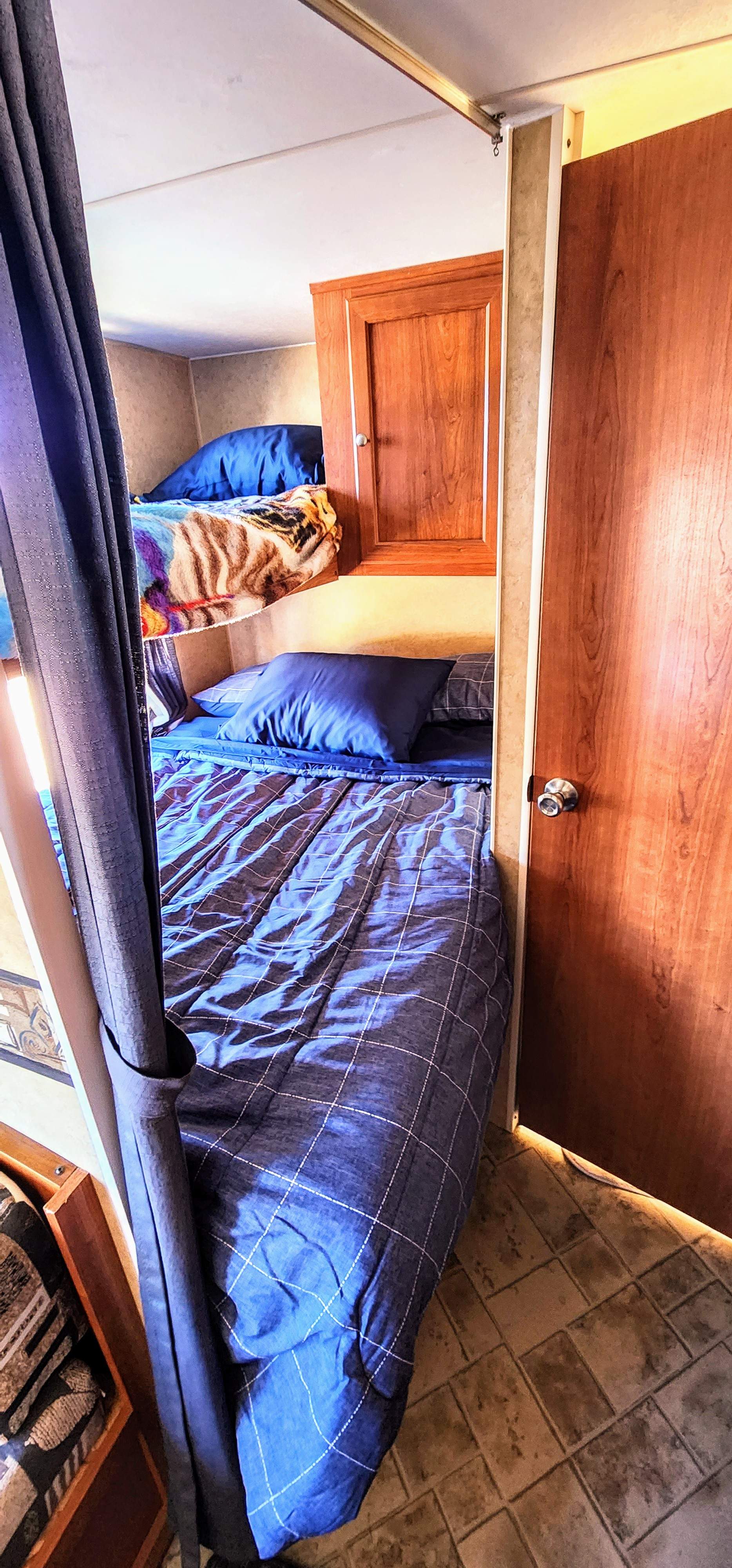 Cozy RV rental bunk beds with blue bedding & wood accents, perfect for family travel.. Sport Sport Trailer 2009