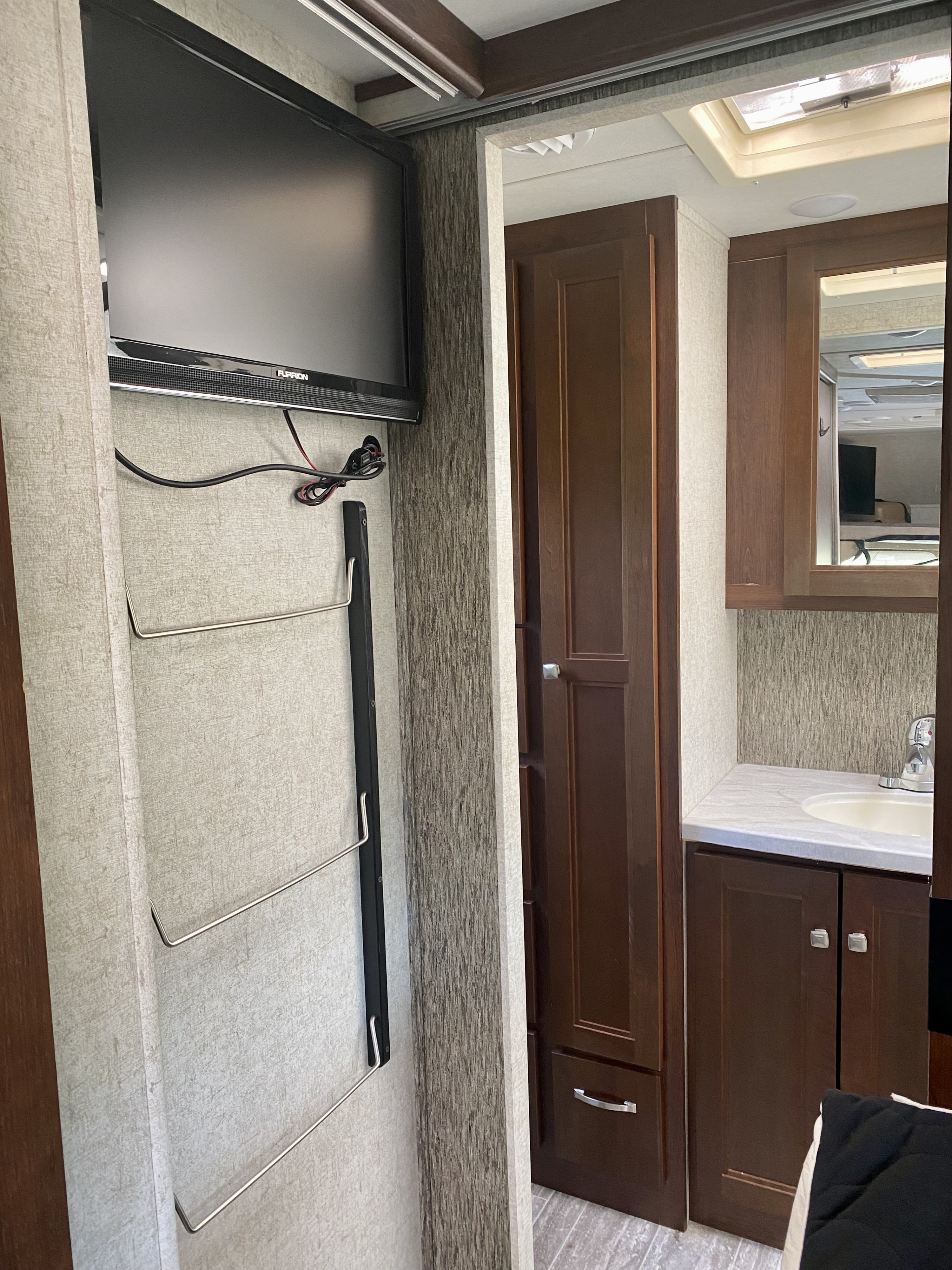 Compact RV rental interior featuring a mounted TV, storage, and a bathroom vanity with a sink and mirror.. Forest River Sunseeker 2018