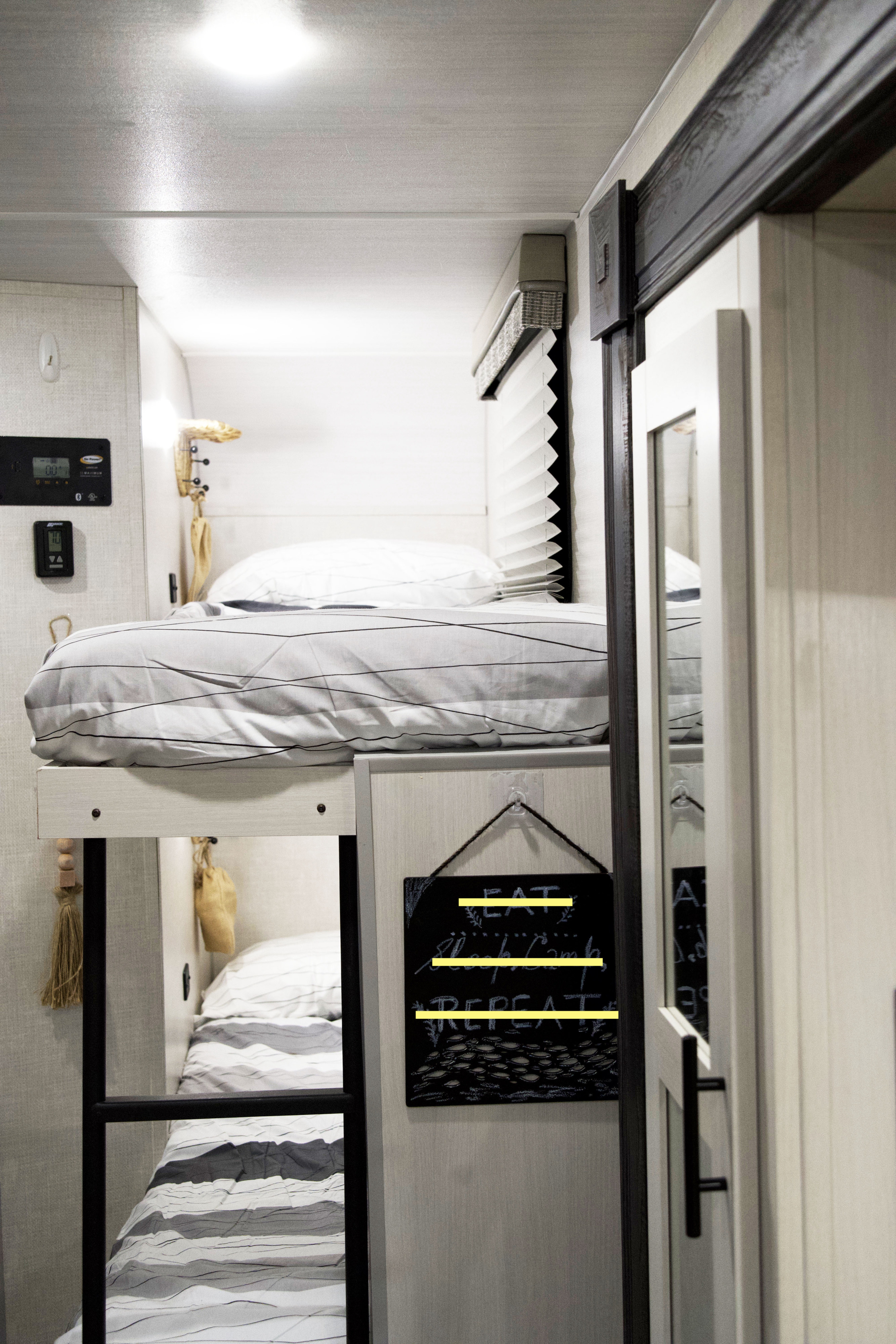 Cozy RV rental interior featuring two comfortable bunk beds with striped bedding, a control panel, and a fun chalkboard sign.. Forest River R-Pod 193 2022