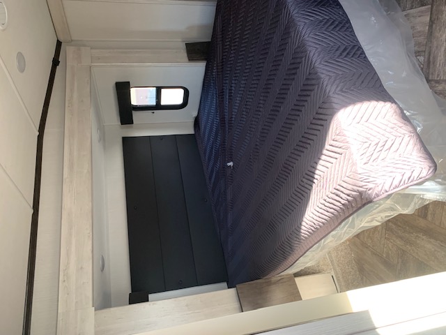 Cozy RV rental bedroom showing a bed with a quilted cover and protective plastic, a small window, and dark headboard.. Forest River Wildcat 2023