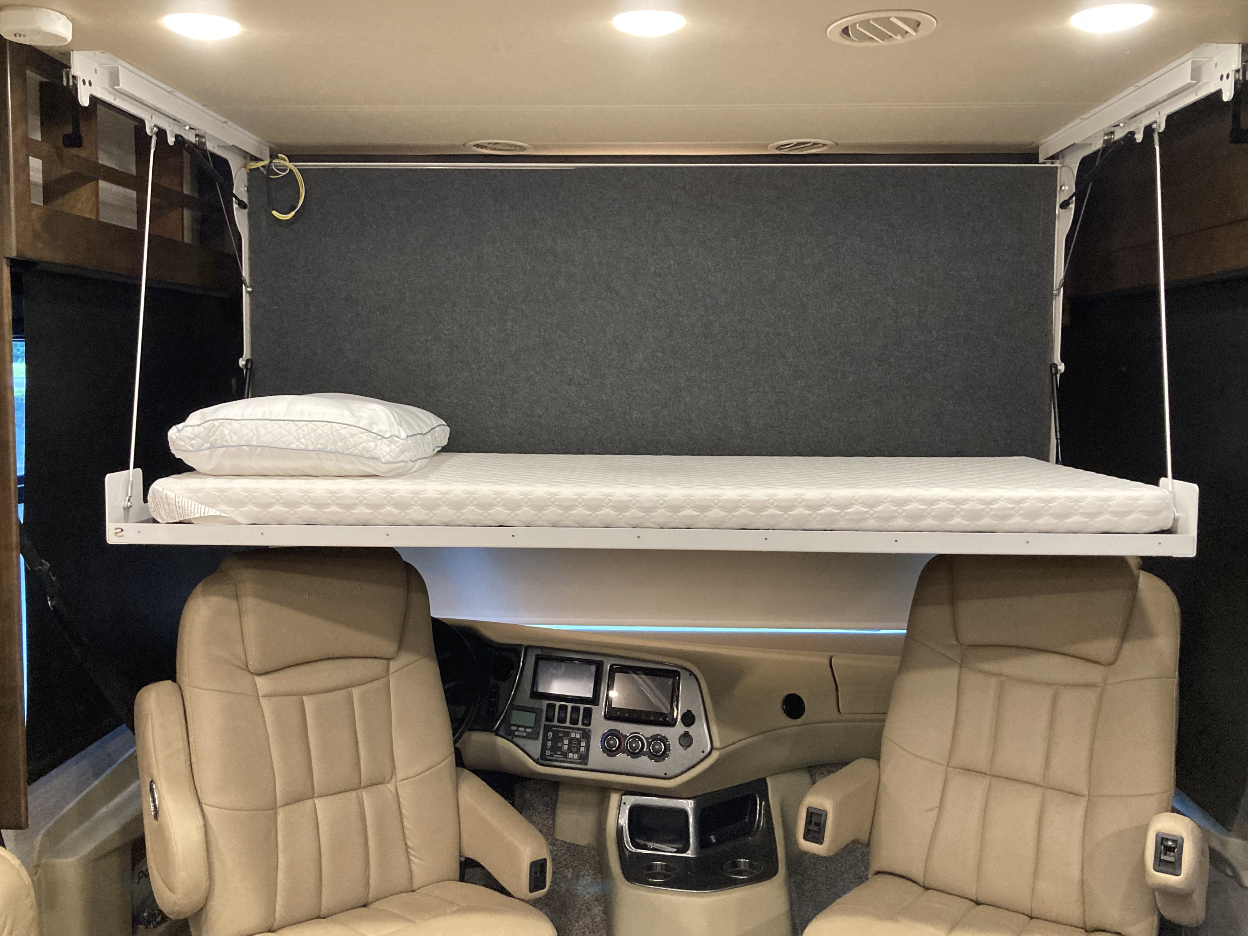 RV rental interior shows a suspended bed with pillow above the vehicle's beige driver and passenger seats.. Allegro Allegro Open Road 2019