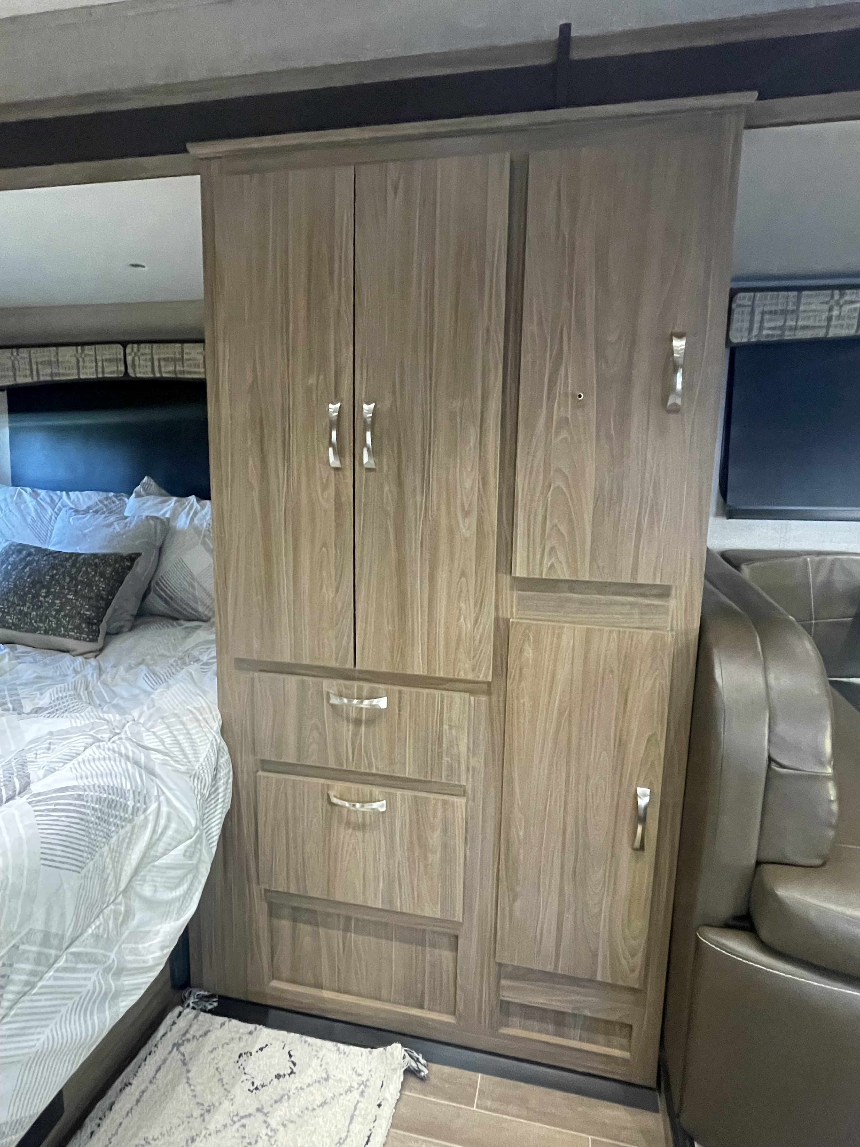 View inside an RV rental: a cozy bed, integrated wood wardrobe with doors & drawers, and adjacent leather seating area.. Isata 3 2018