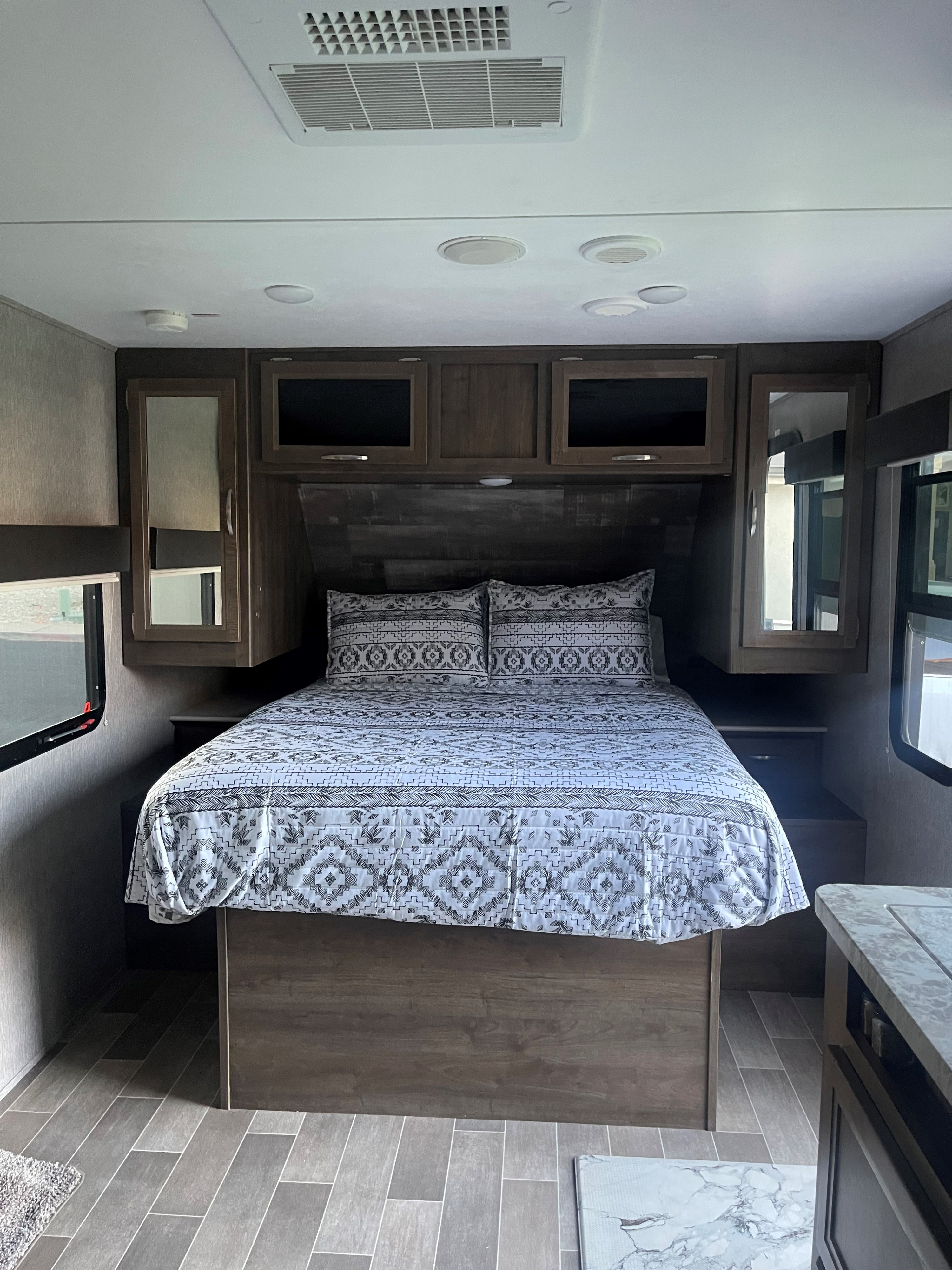 Inside an RV rental bedroom: cozy bed with patterned linens, wood-toned cabinets, and an overhead AC unit for comfort.. Dutchmen Coleman Light 2019