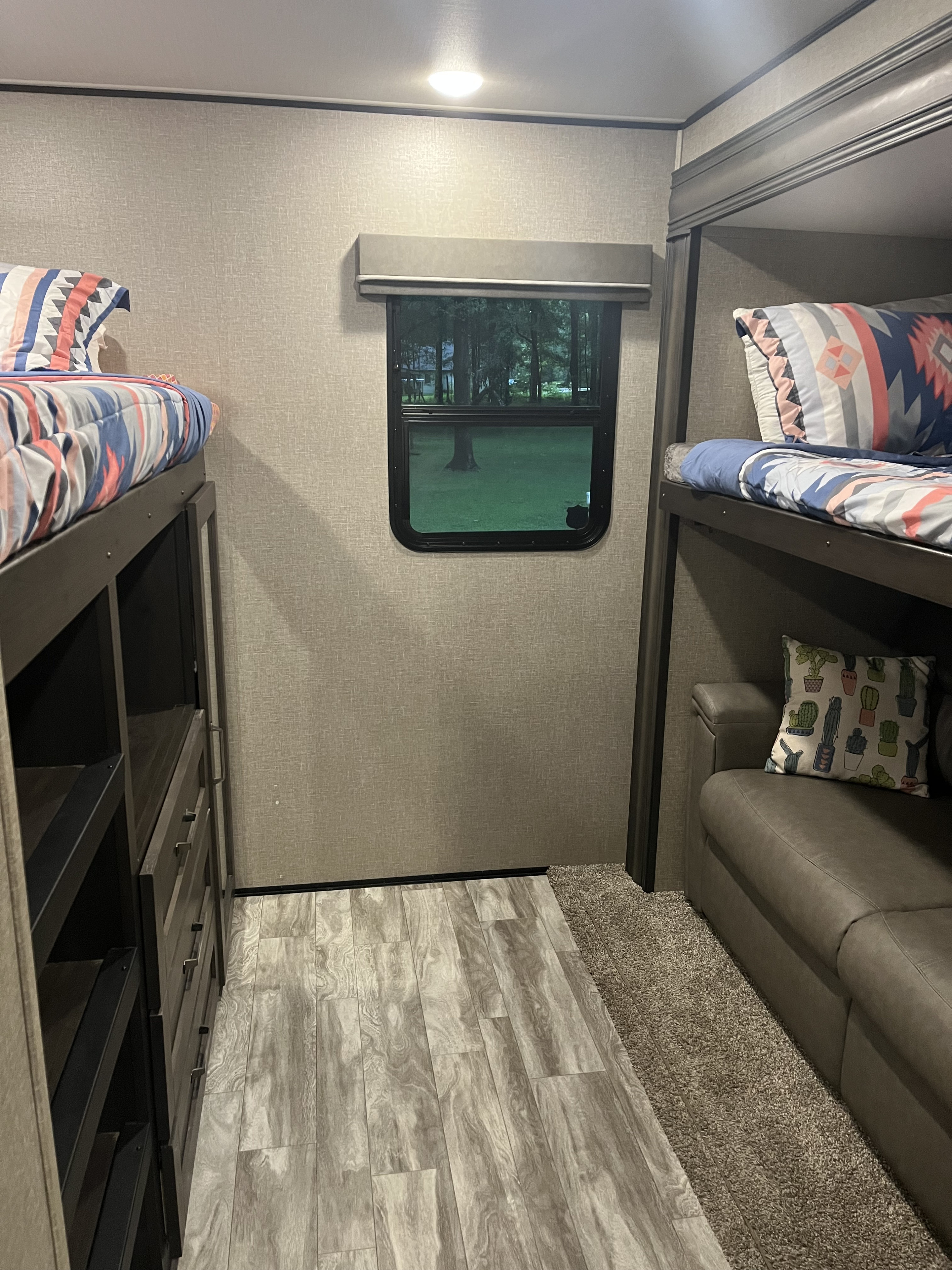 Inside an RV rental bunkhouse: cozy bunk beds with colorful linens, storage, a sofa, and a scenic window view.. Grand Design Reflection 2020