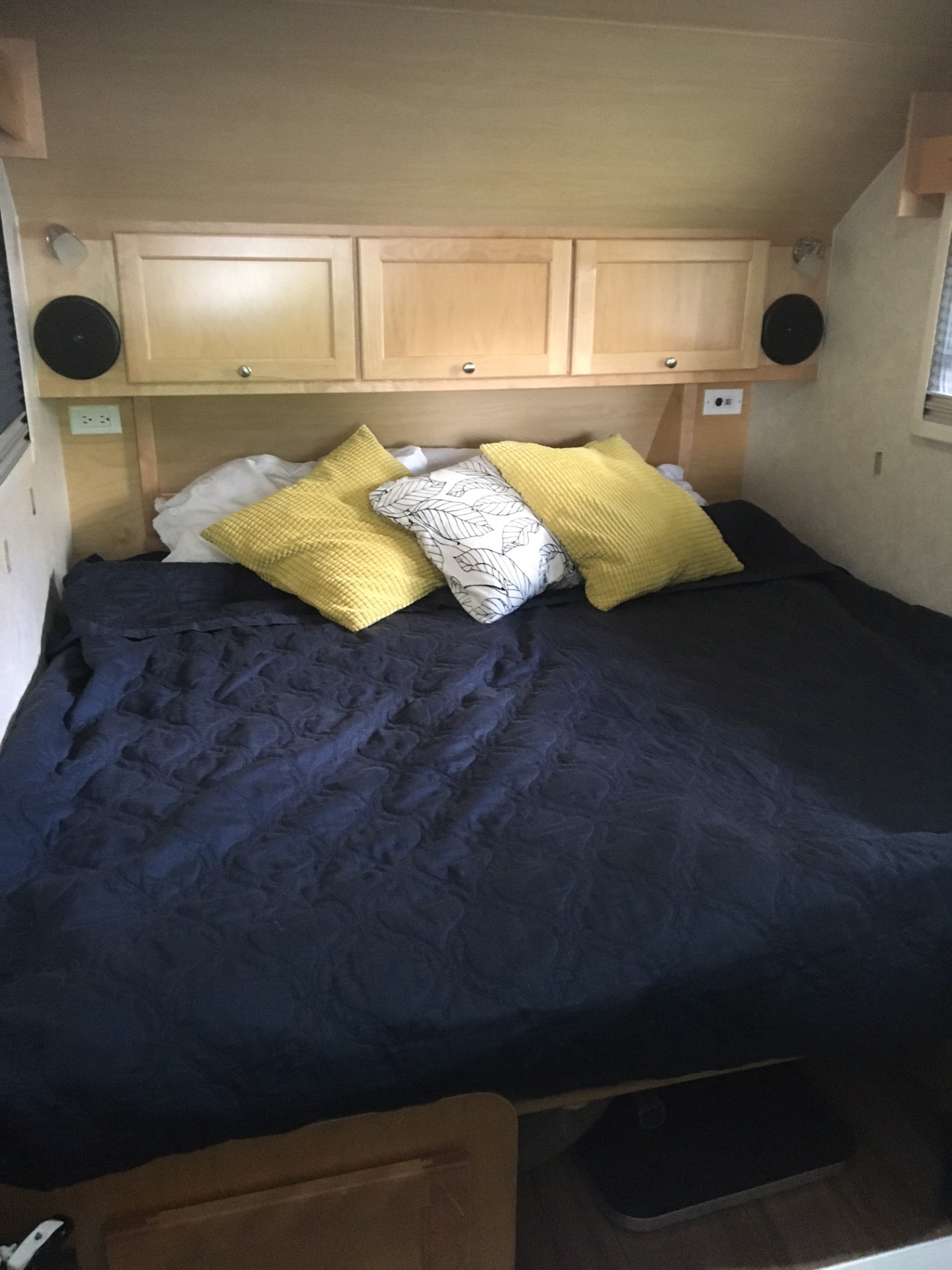 Cozy RV rental bedroom with dark blue comforter, bright pillows, and convenient overhead storage.. nuCamp T@B 2019