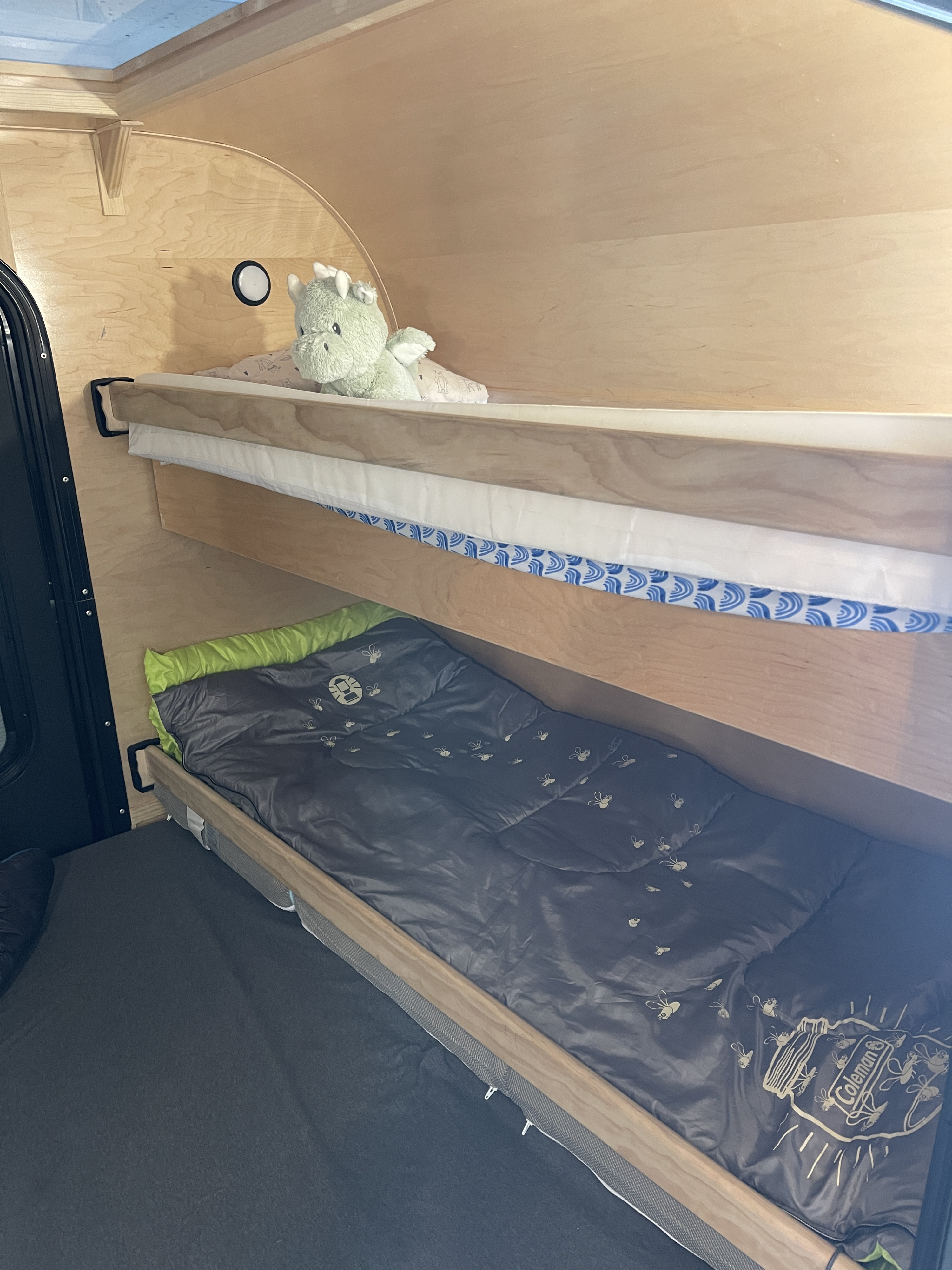 Cozy bunk beds inside an RV rental, with a stuffed dragon on the top bunk and a Coleman sleeping bag below. Ideal for camping.. Other Other 2022