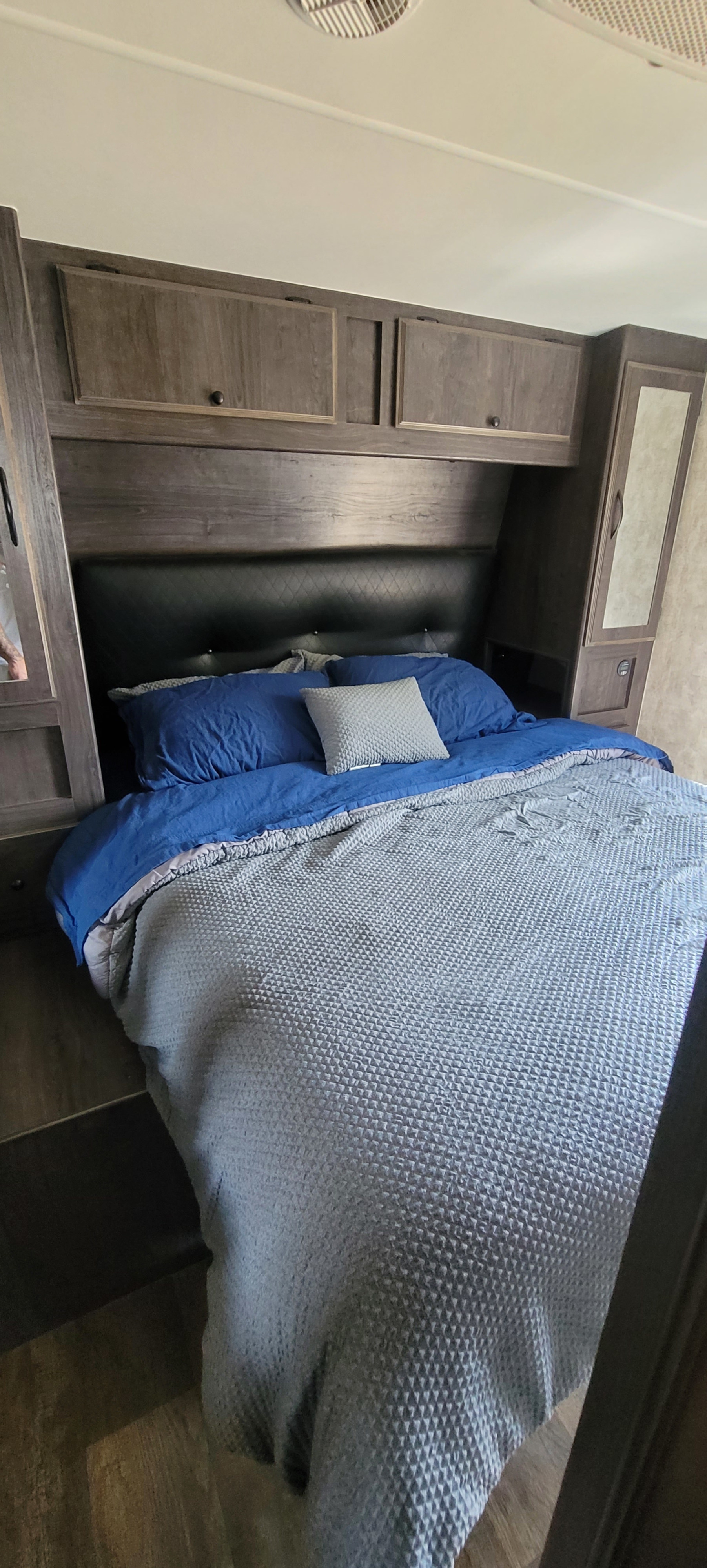 Cozy RV rental bedroom featuring a bed with blue and gray textured bedding, an upholstered headboard, and wood cabinets.. Eclipse Recreational Vehicles Iconic 2018