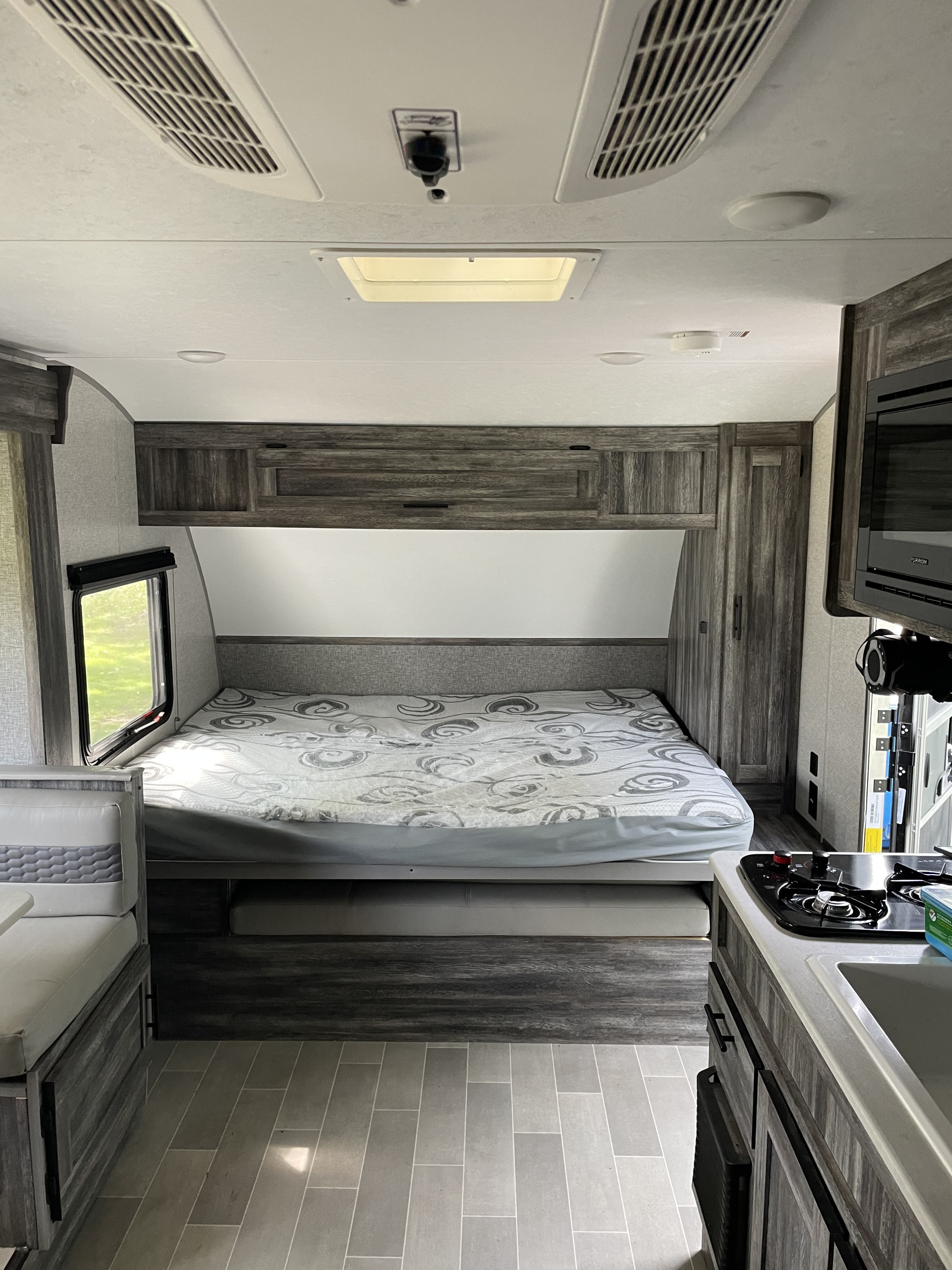 Modern RV rental interior: A compact bedroom with bed, overhead storage, window, and kitchen.. Forest River Salem FSX 2020