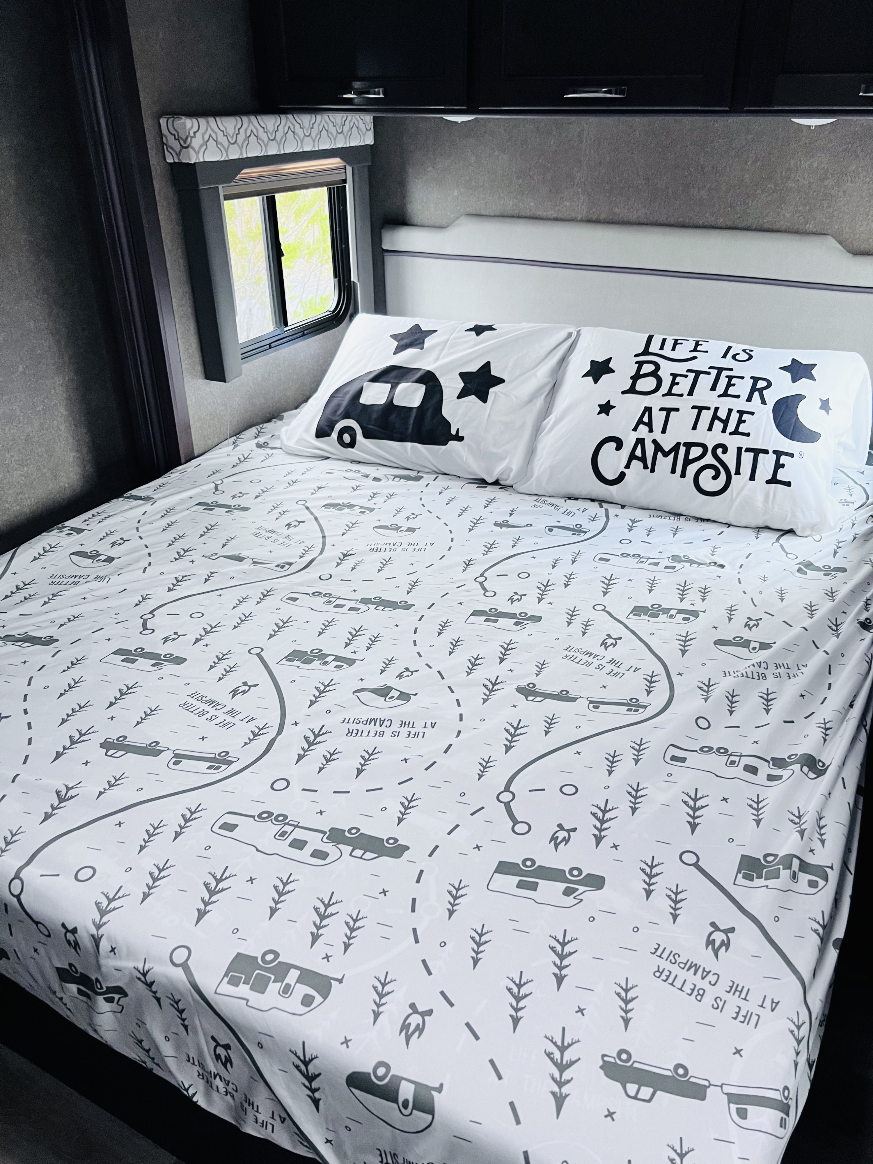 Cozy RV rental bed with fun "Life is Better at the Campsite" bedding featuring camper and tree patterns. Perfect for road trips!. Thor Freedom Elite 2020