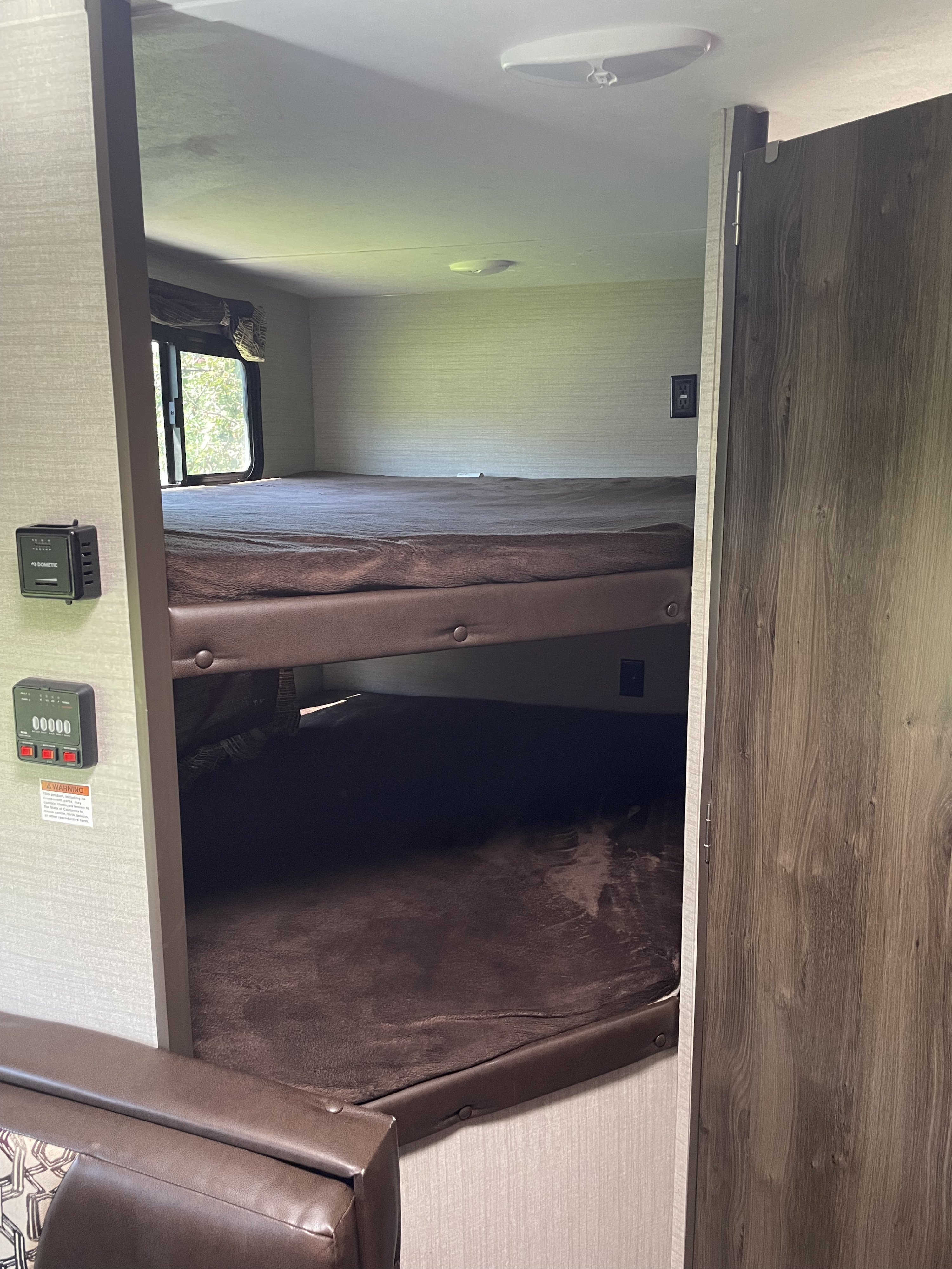 Inside an RV rental, featuring bunk beds with brown blankets, a window, and control panels for a comfortable mobile sleeping space.. Keystone RV Bullet Crossfire 2019