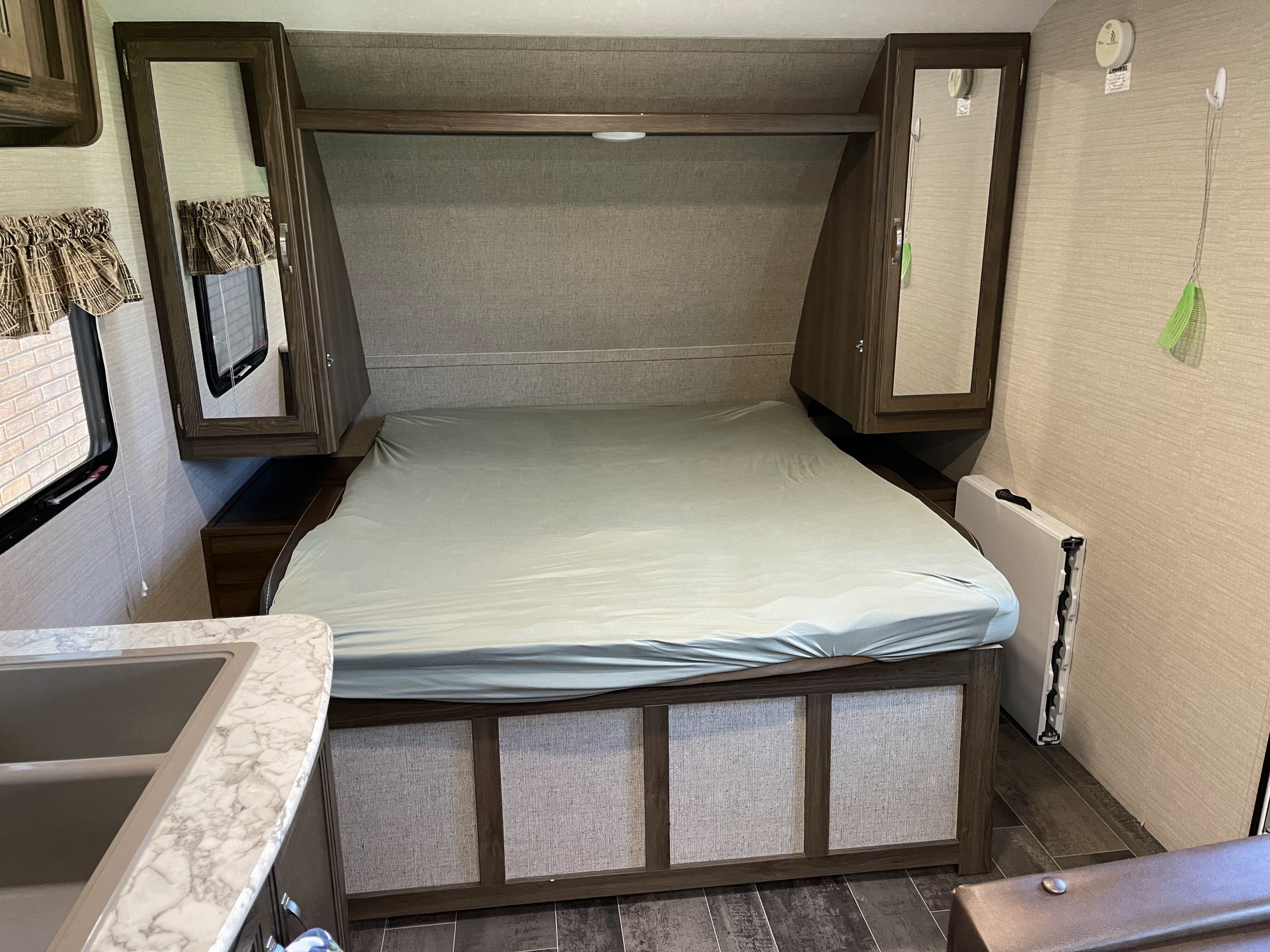 RV rental bedroom: cozy bed, overhead mirrored cabinets, compact kitchen sink, and patterned window in a camper.. Keystone RV Bullet Crossfire 2019
