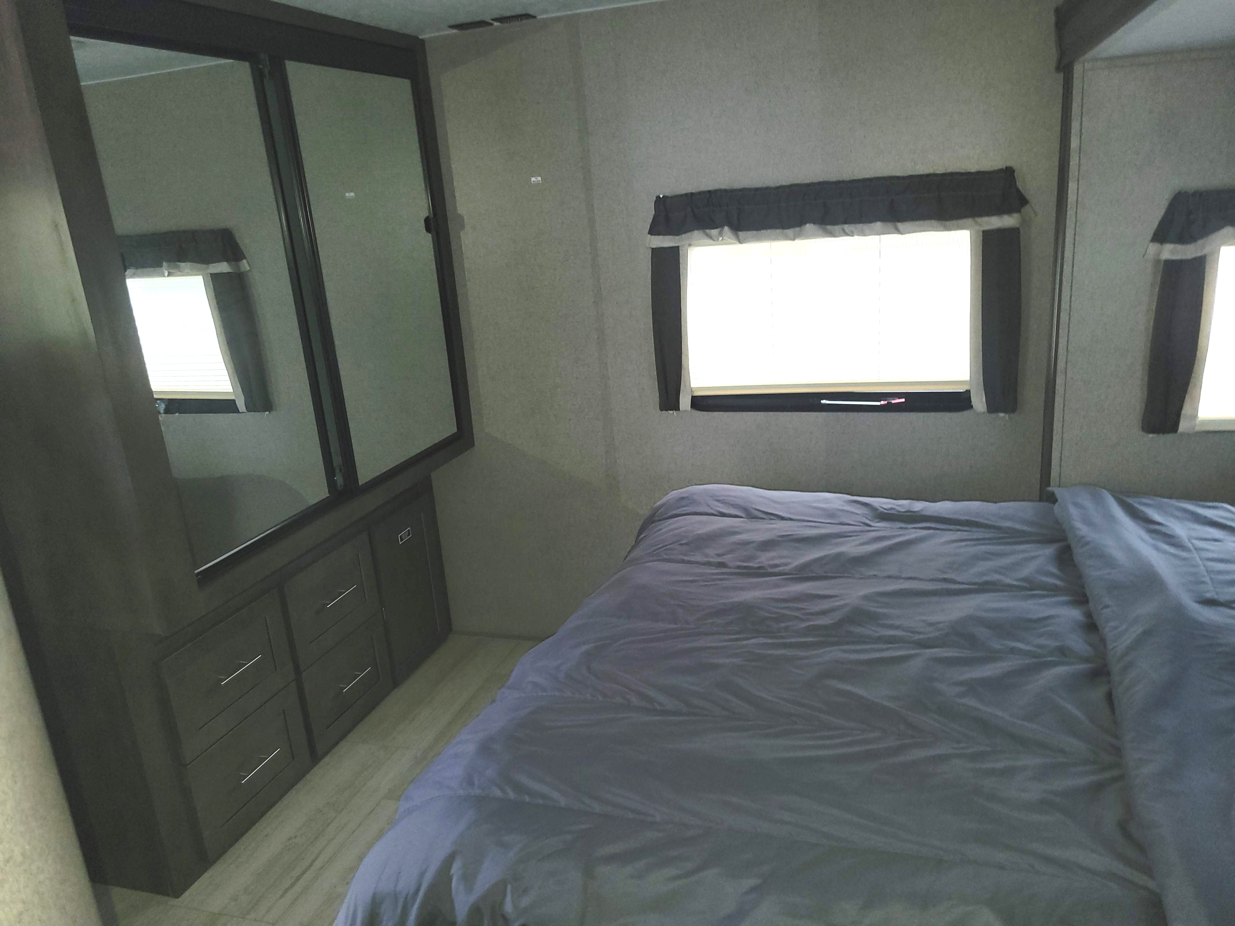 Cozy RV rental bedroom featuring a comfortable gray bed, two curtained windows, and a mirrored closet/dresser unit for storage.. Forest River Rockwood Ultra Lite 2020