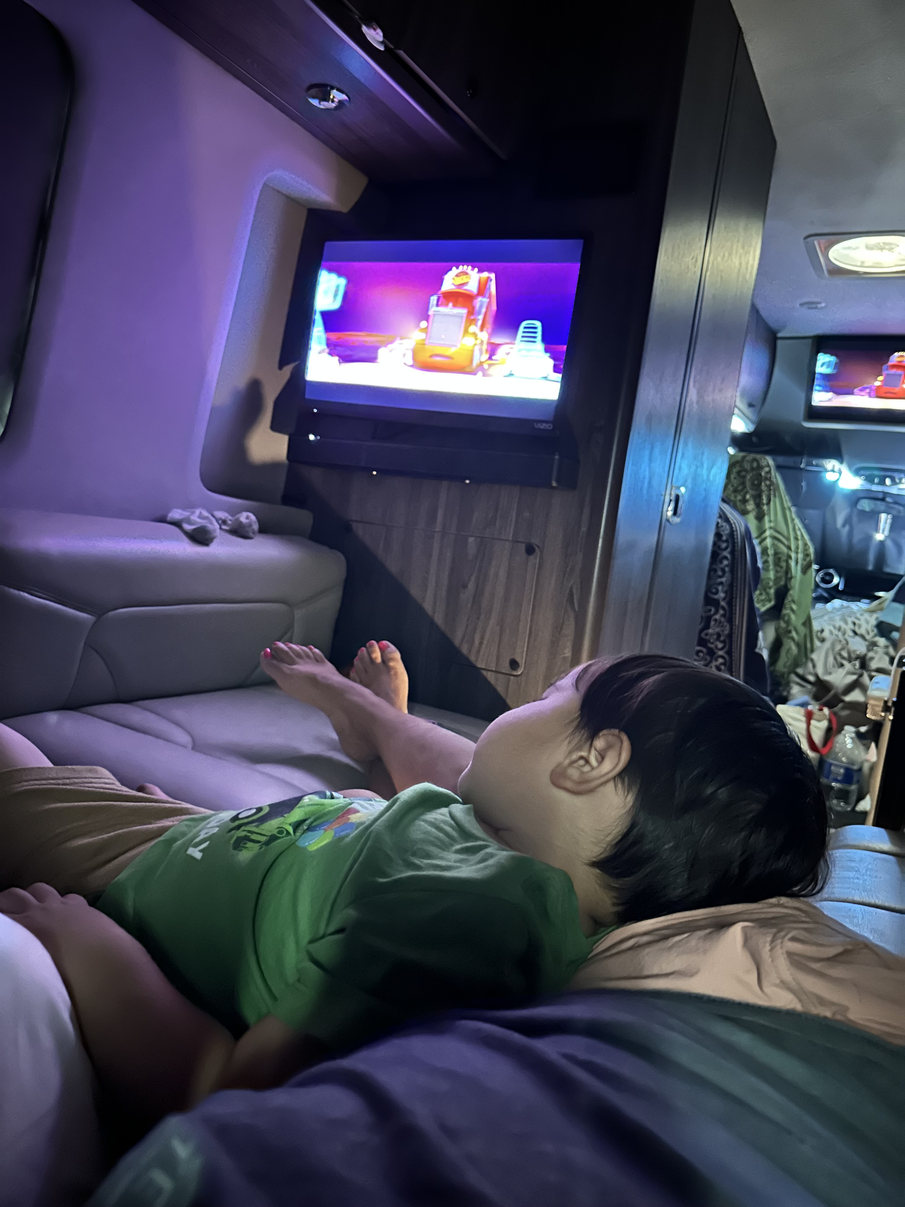 Inside an RV rental, a child relaxes and watches a cartoon on TV, showing a cozy, dim-lit interior.. Grech Motors Strada 2022