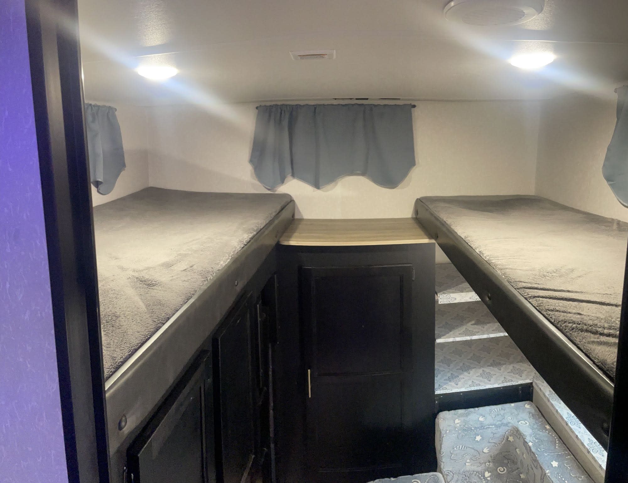 RV rental bunk bed sleeping area. Two bunk beds with gray blankets, central storage, and patterned steps for access.. Forest River Cherokee Grey Wolf 2021