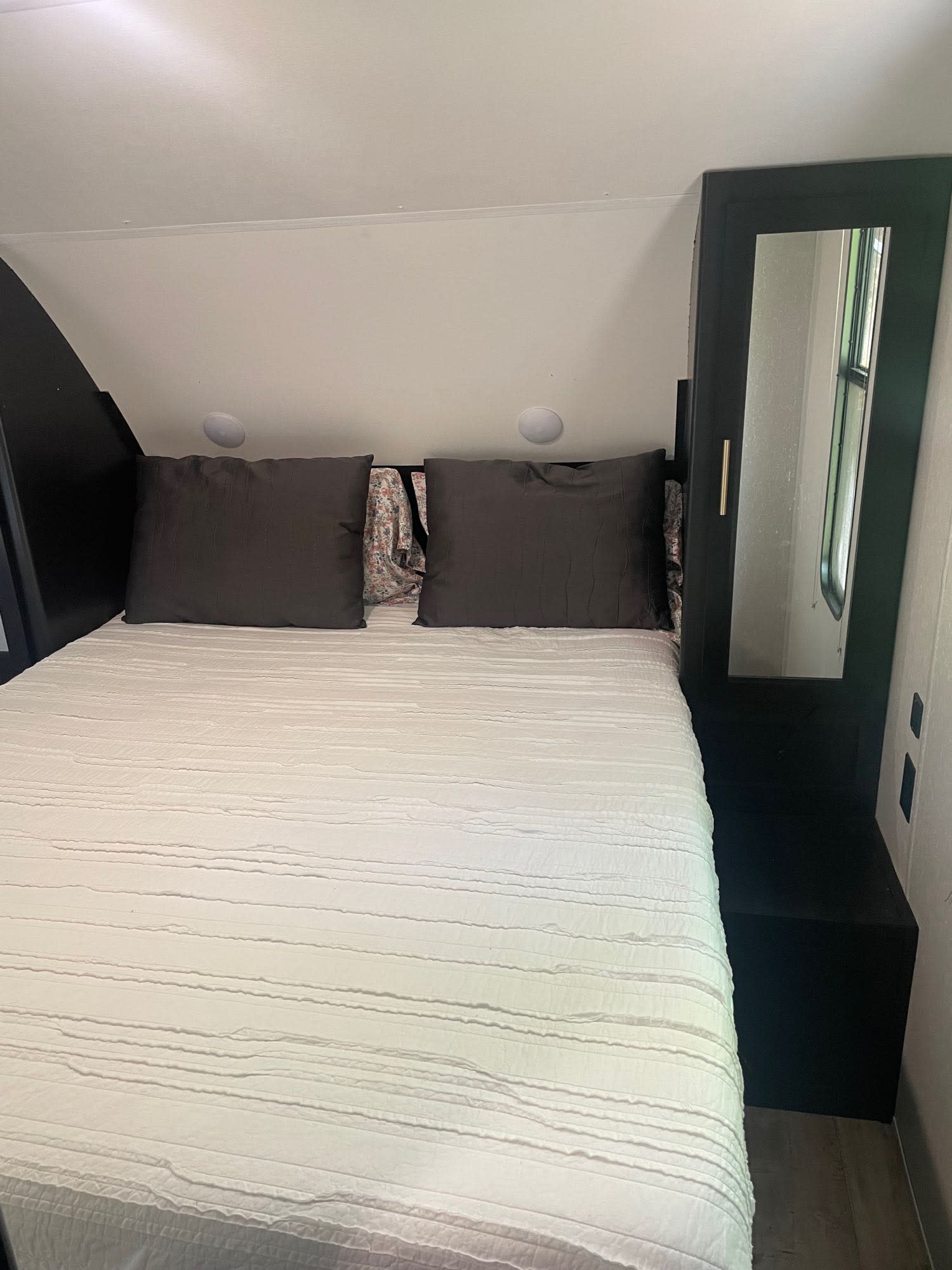 Compact RV rental bedroom featuring a queen bed, integrated storage, and a mirror. Ideal for cozy travels.. Forest River Cherokee Grey Wolf 2021