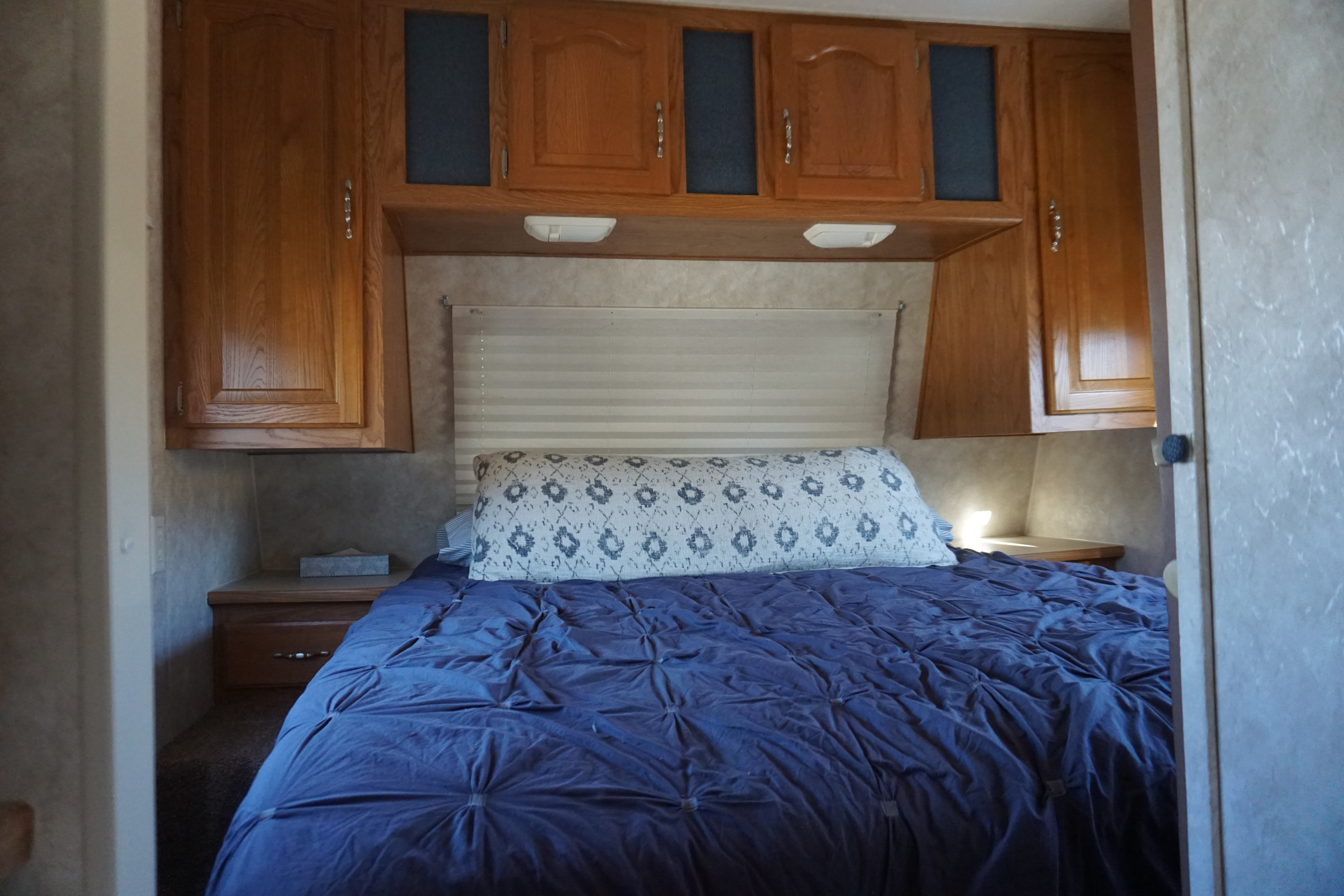 Inside an RV rental, this bedroom features a comfy bed with blue bedding, a patterned pillow, and ample wooden storage cabinets.. Keystone RV Sprinter 2004