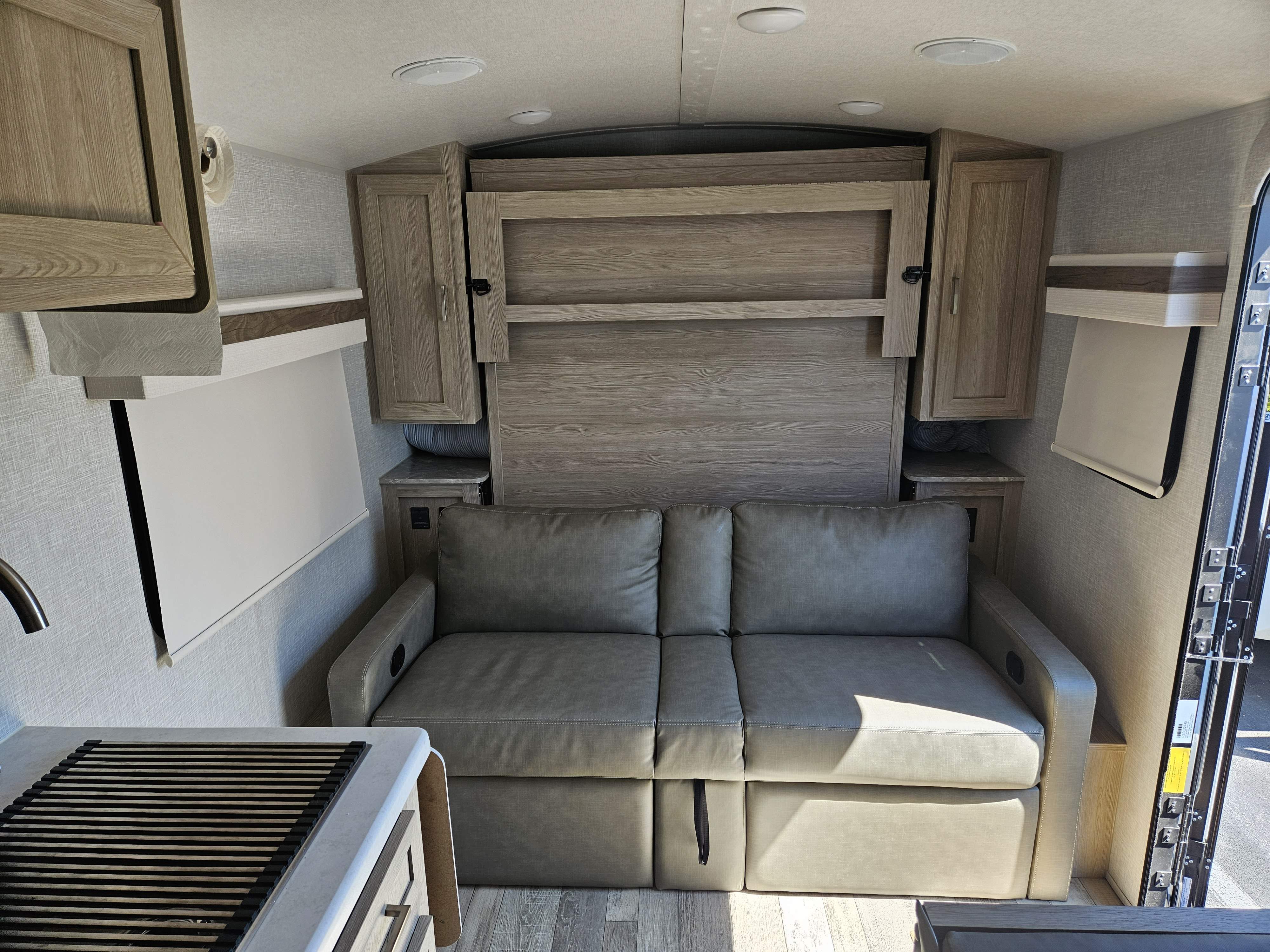 RV rental interior showcasing a gray pull-out sofa, integrated murphy bed, and compact kitchenette for travel.. Forest River Rockwood Geo Pro 2022